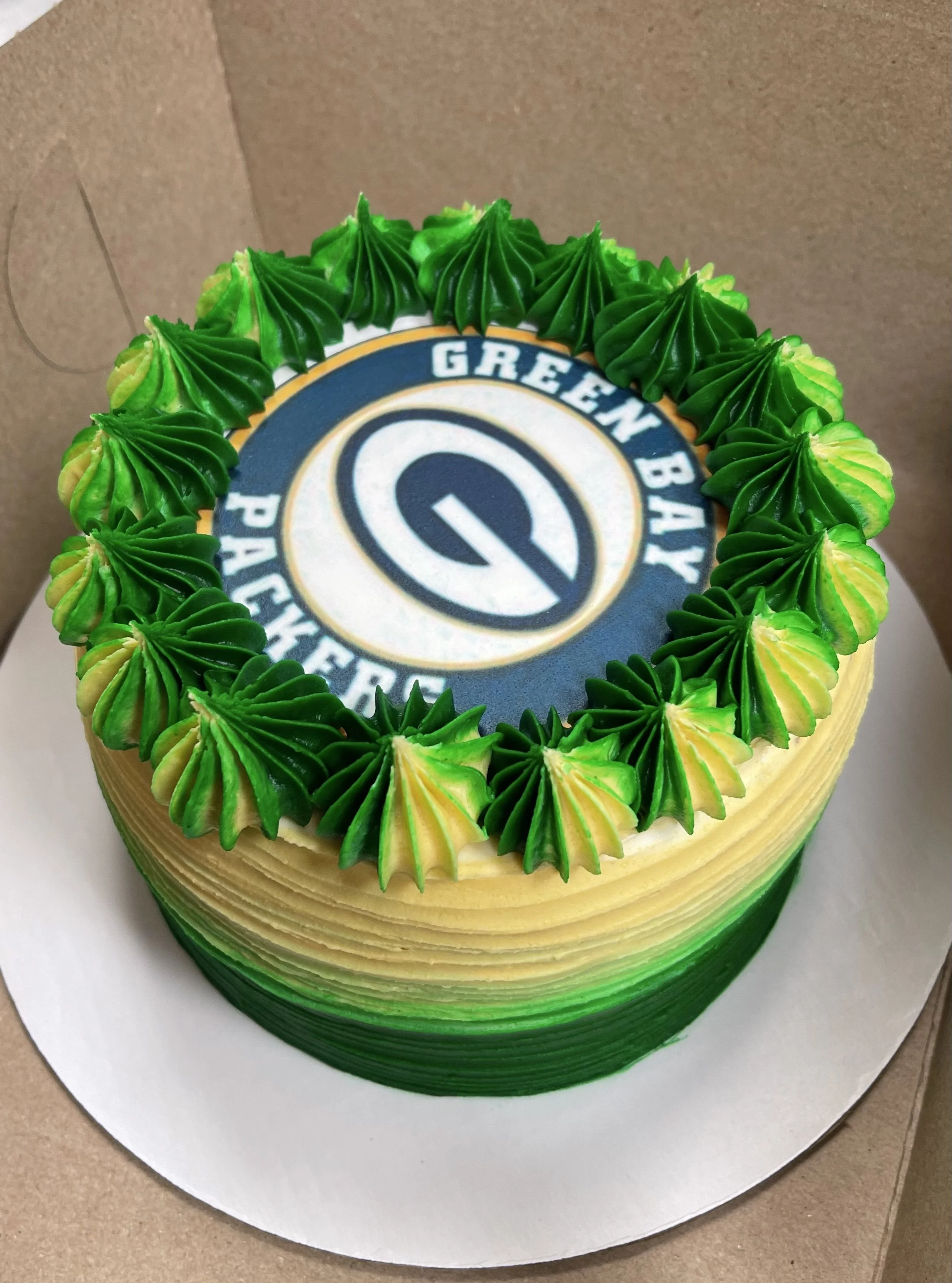 A cake with green and yellow frosting, featuring the Green Bay Packers logo on top.