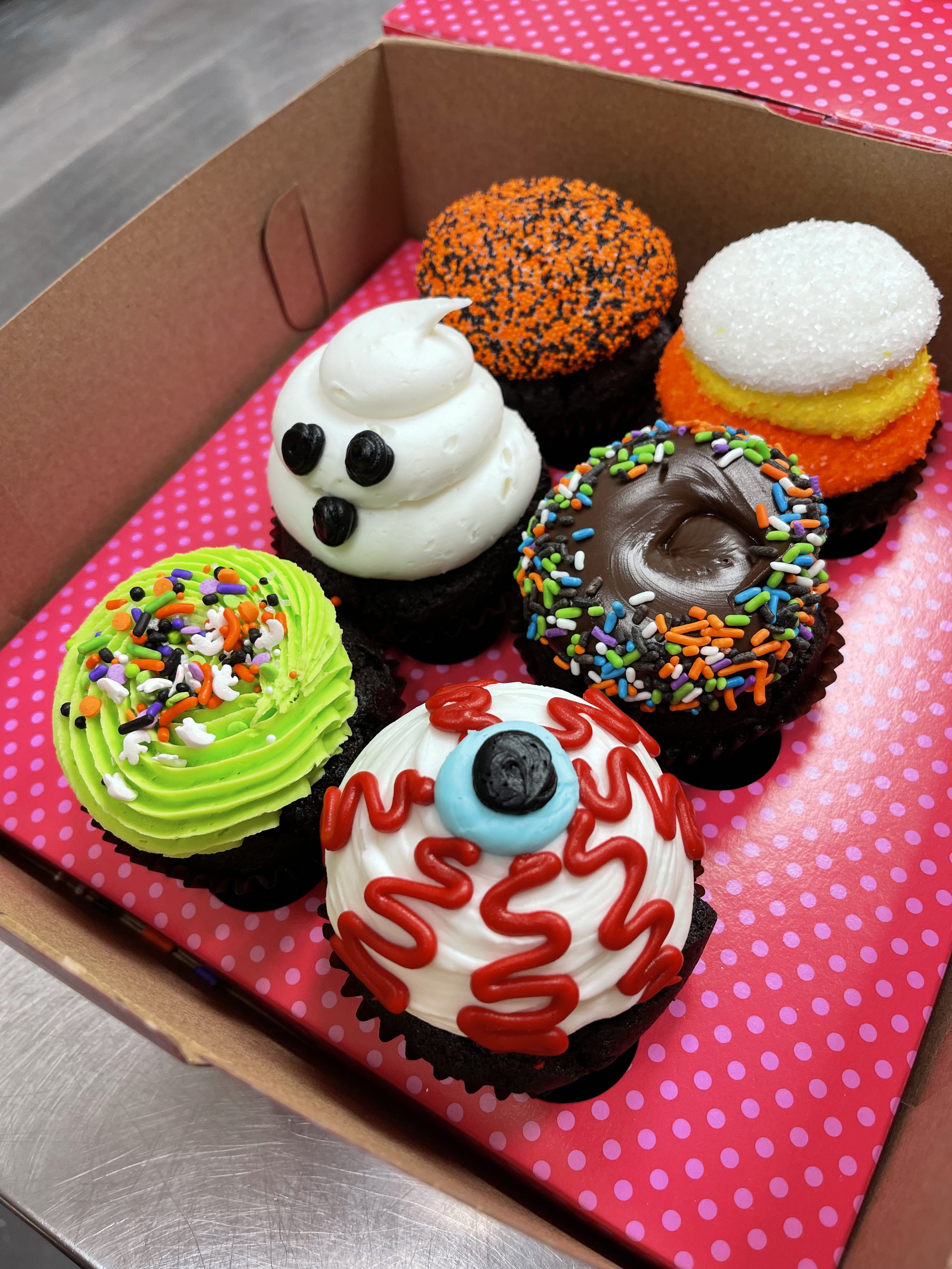 Assorted Halloween-themed decorated cupcakes in a pink polka dot box