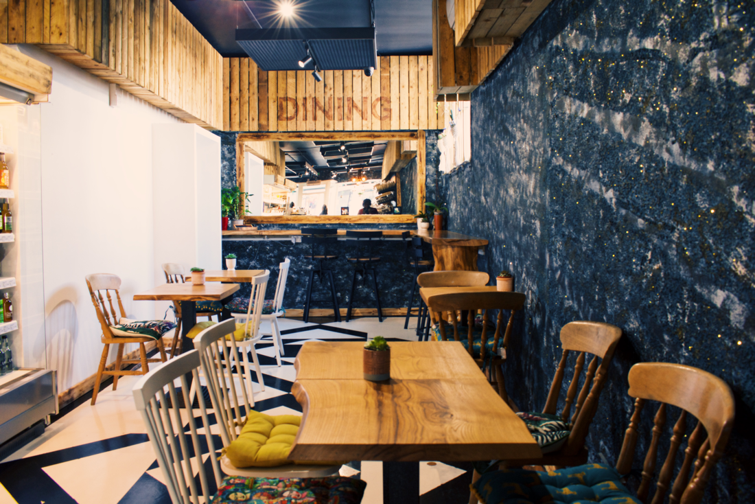 Cozy cafe interior with wooden tables, a navy and gold accent wall, and a bar area in the background.
