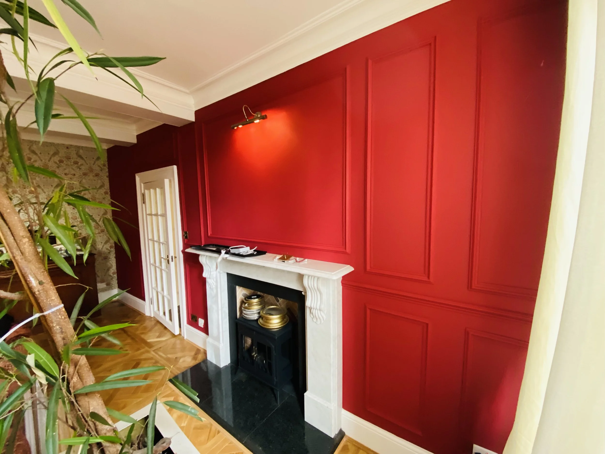 Red feature wall with decorative panelling and fireplace in a living room, professionally painted and decorated in Hertfordshire.