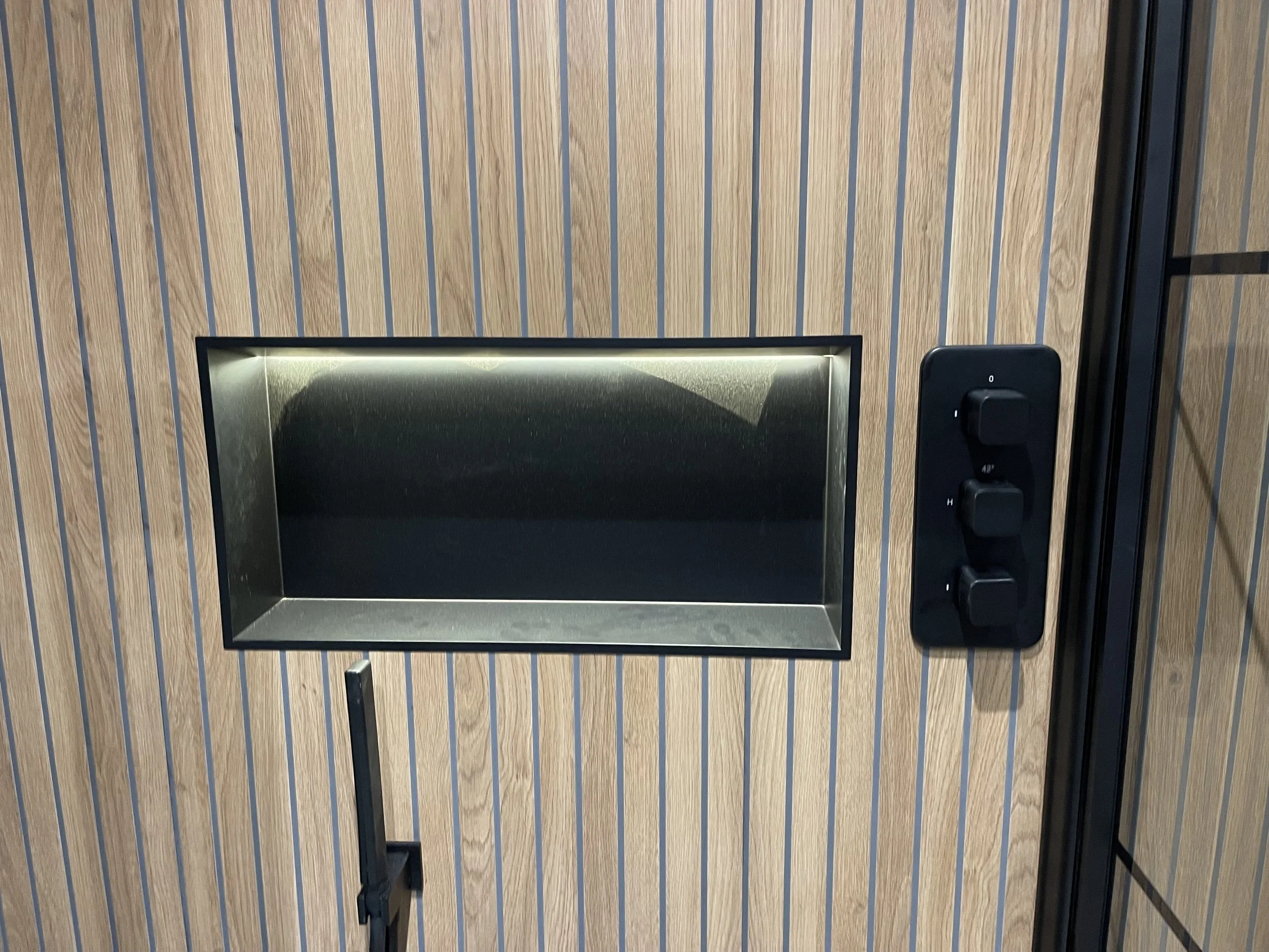 Wooden wall with a rectangular stainless steel opening and a black control panel with three switches to the right of the opening.