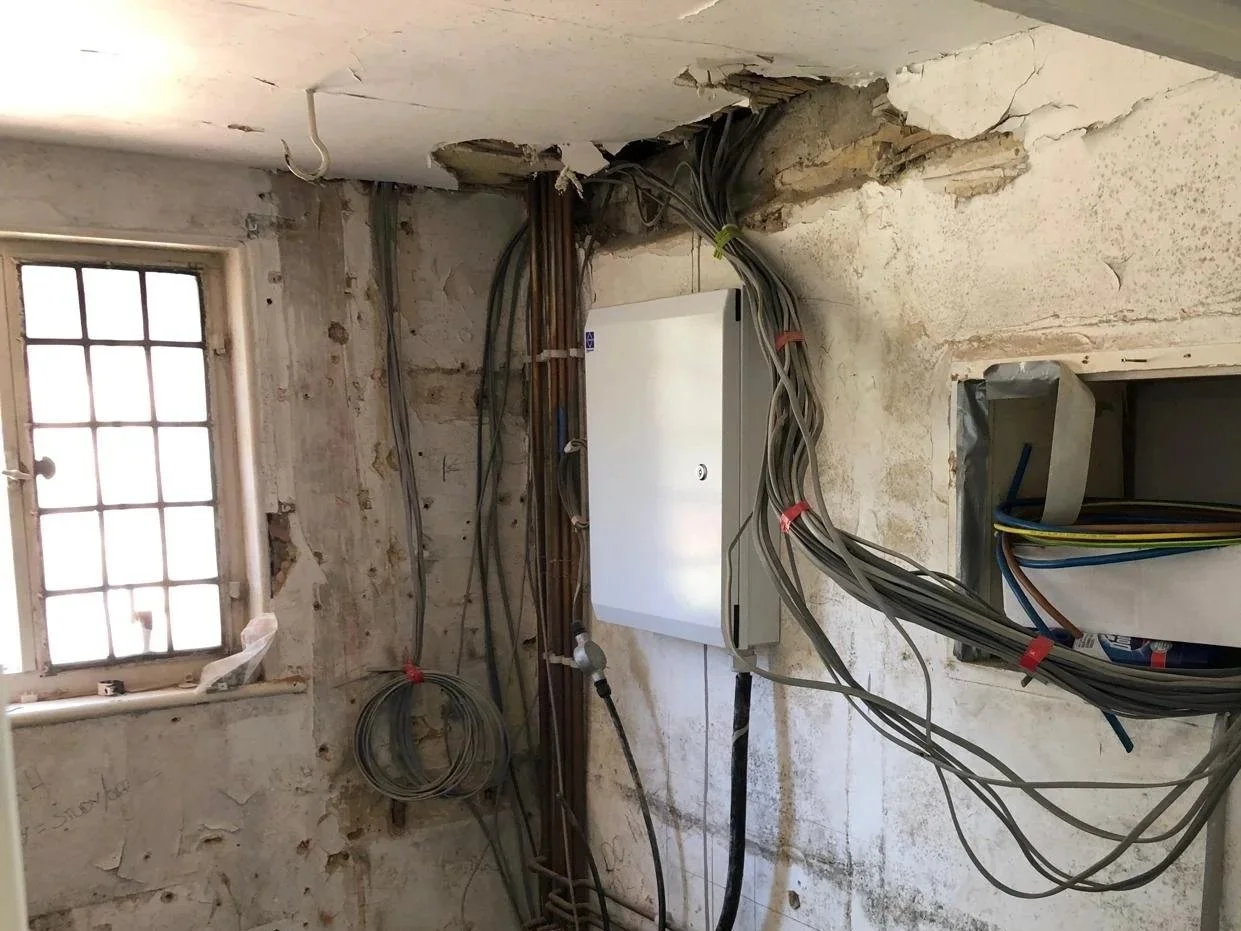 Interior wall with exposed electrical wiring, a junction box, a window, and an unfinished surface.