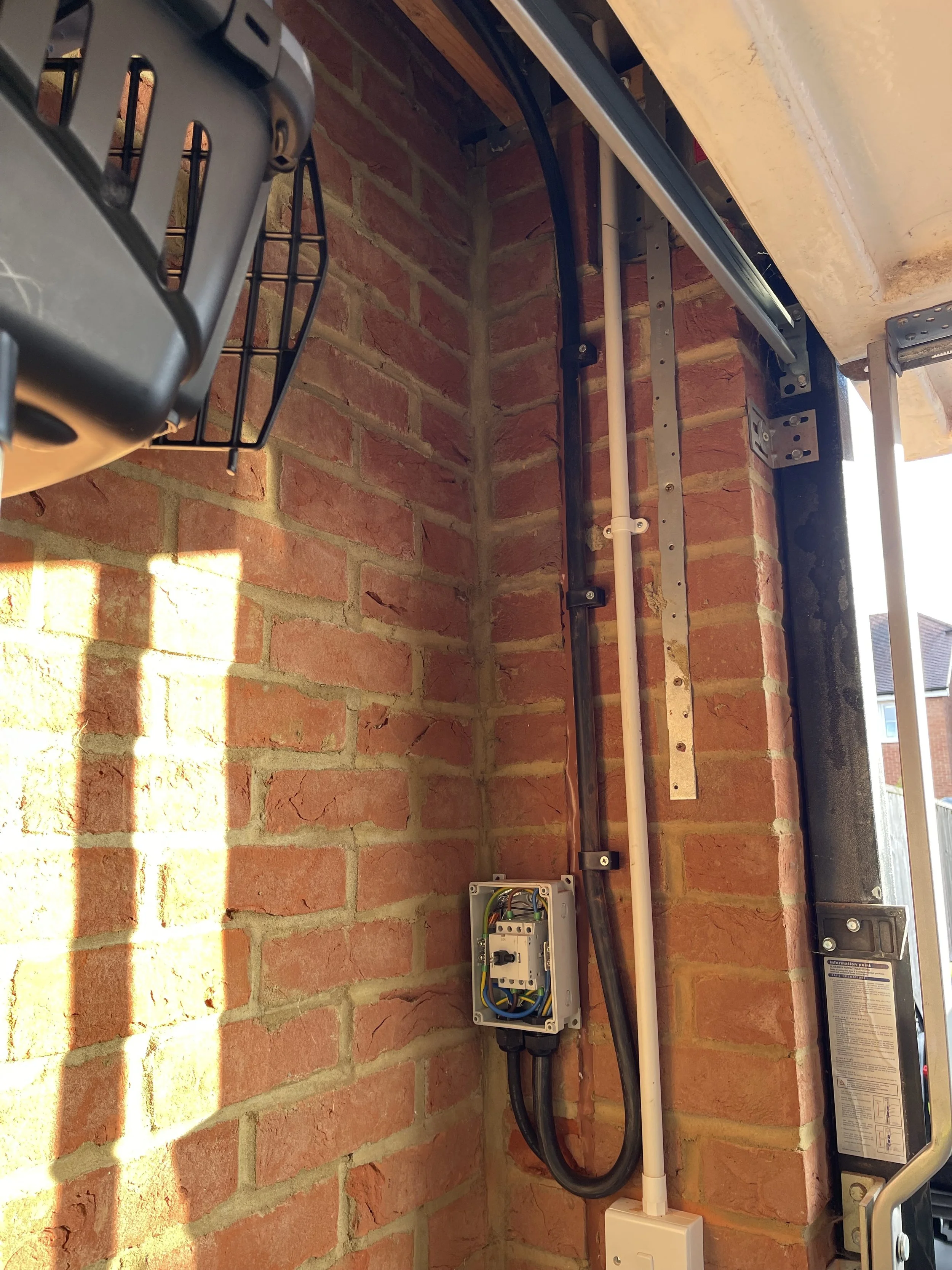 Close-up view of electrical wiring and conduit running along a brick wall, with an electrical junction box visible at the bottom, containing circuit wiring.