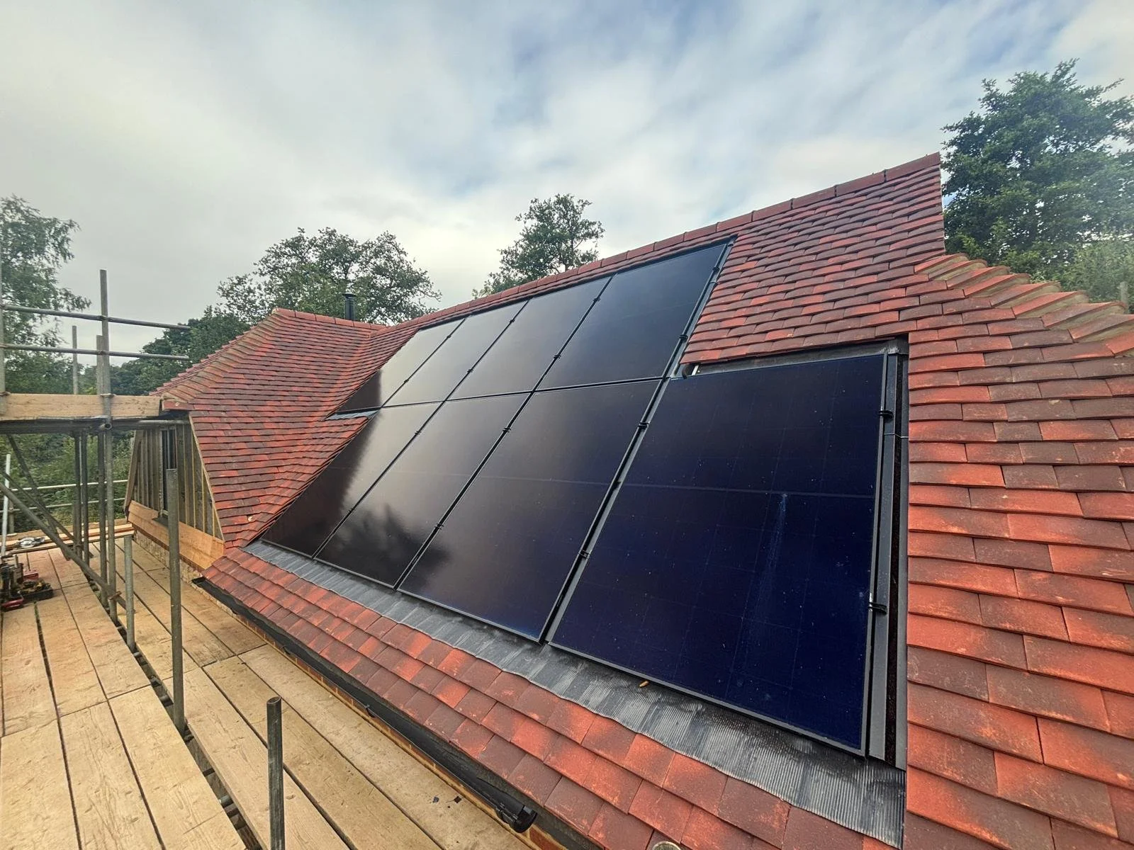Solar panels installed on a red tiled roof of a house under construction with scaffolding around.