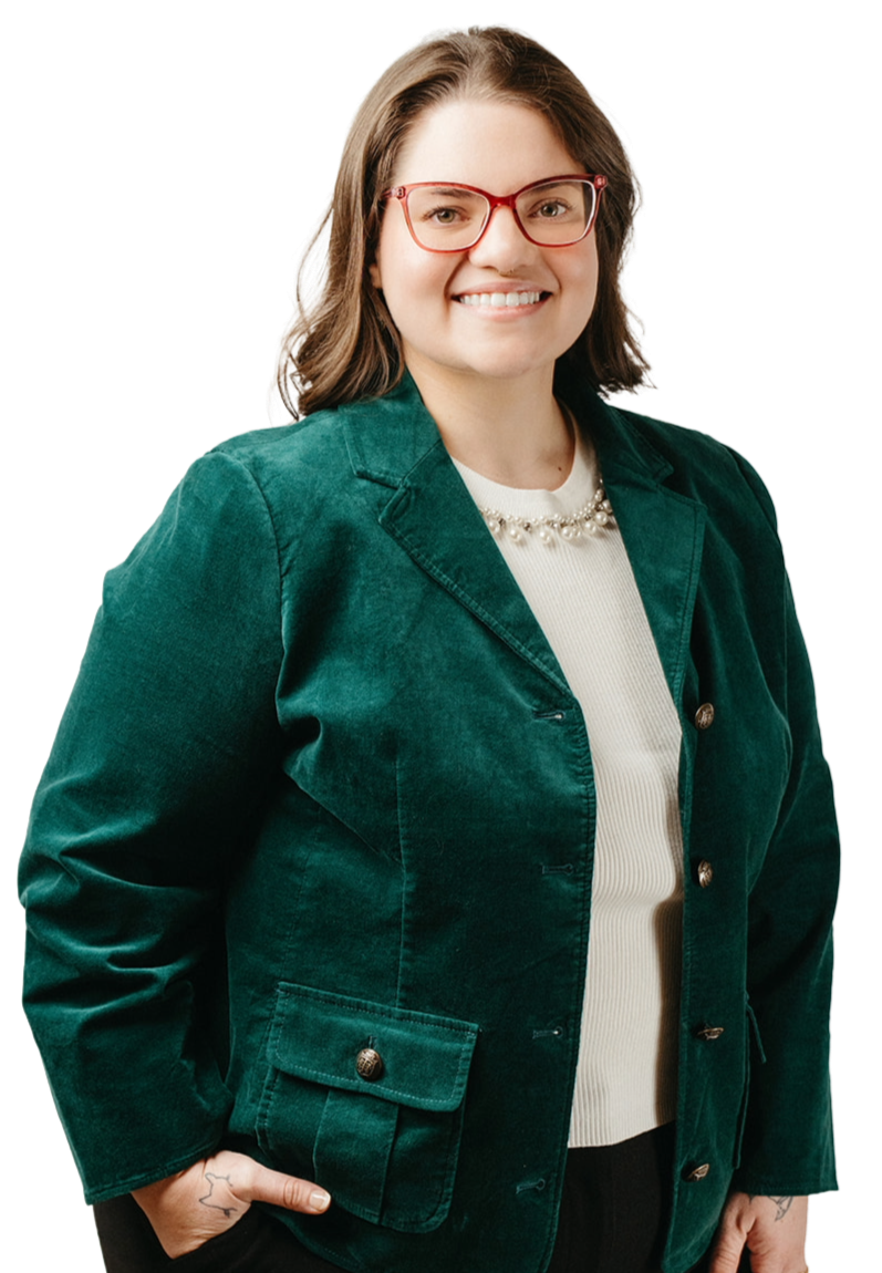 A woman with shoulder-length brown hair wearing red glasses, a white top with a pearl necklace, and a green jacket, smiling at the camera.