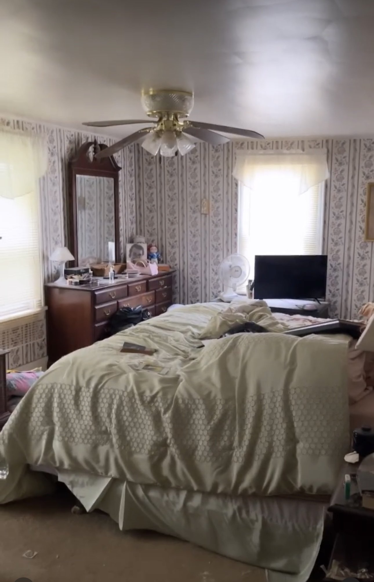 Unkempt bedroom with an unmade bed, dresser with mirror, television, and clutter on furniture.