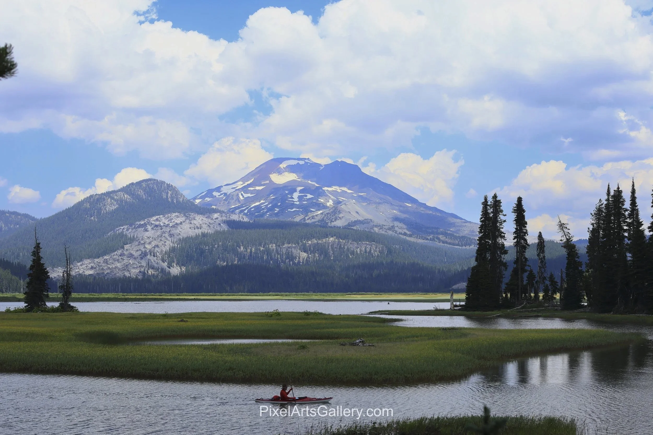 Mountain Marsh - 

A lone kayaker in a red boat crosses a quiet channel bordered by green marsh grasses. Forested hills and a snow-patched Cascade peak rise beyond.