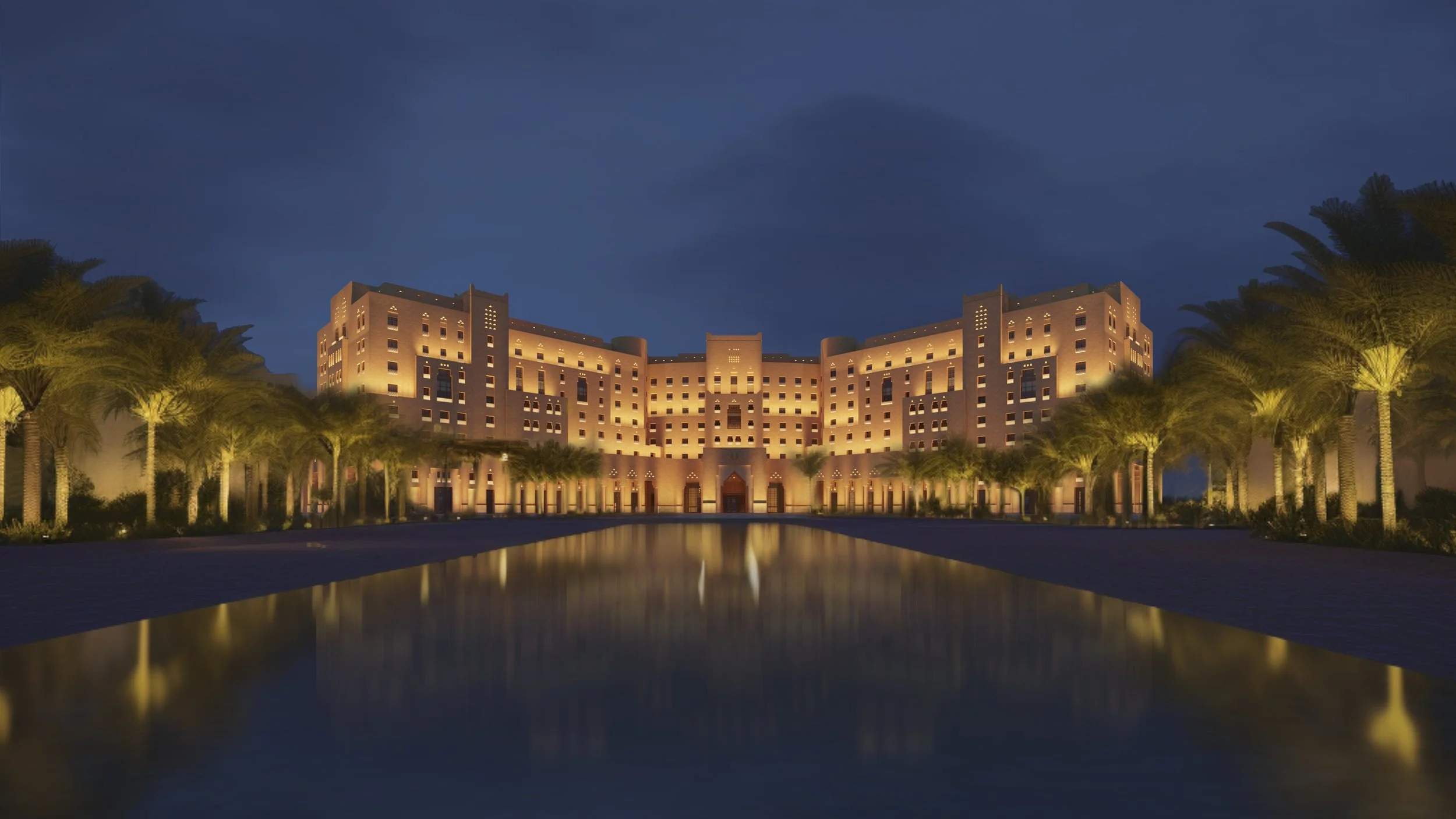 A large hotel or resort building illuminated at night, with a reflecting pool and palm trees in front.