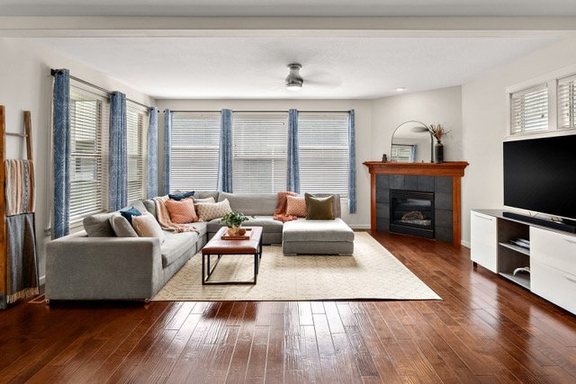 Living room with a sectional sofa, coffee table, TV, fireplace, and large windows with curtains.