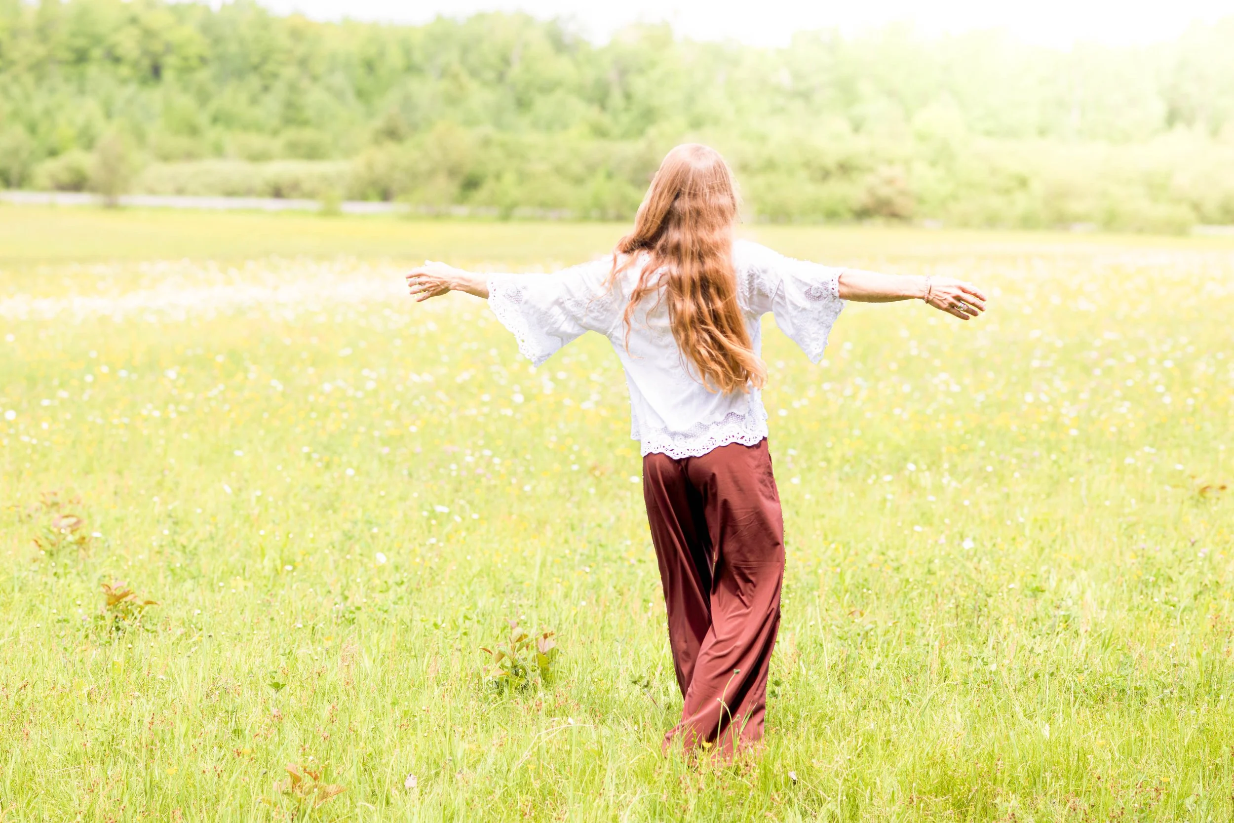 Kristin standing in a peaceful meadow with arms outstretched, embracing growth and new possibilities.