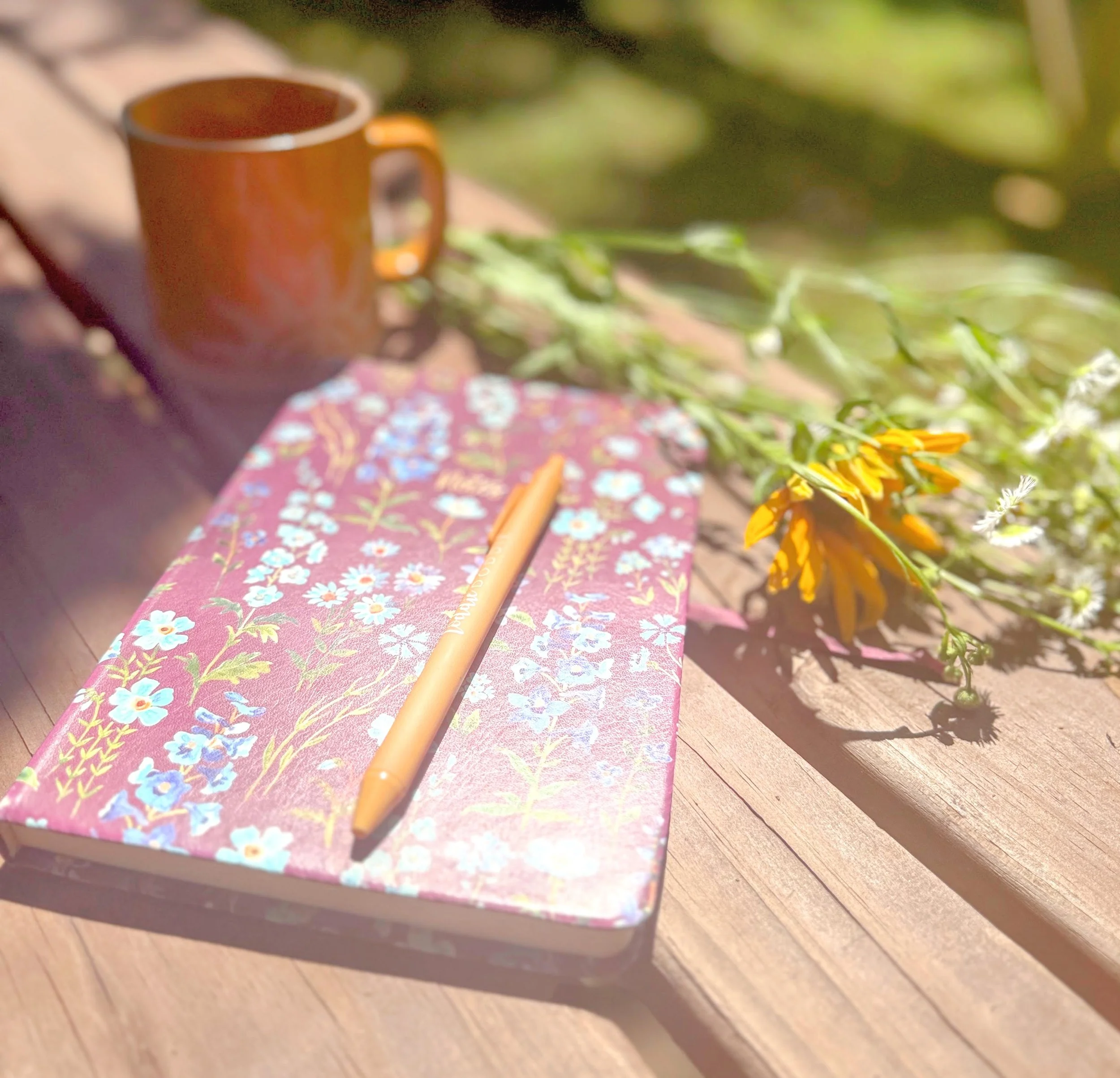 Journal, pen, flowers, mug and tea representing reflection, personal growth, and intentional living.