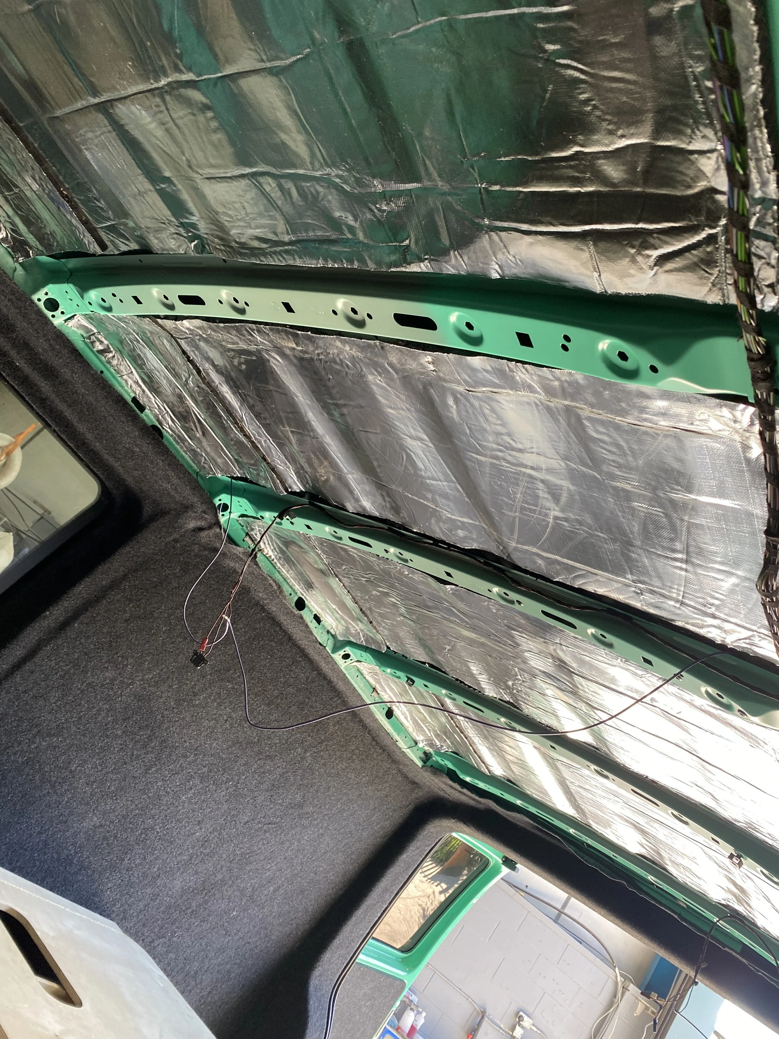 The interior roof of a vehicle under construction, showing shiny insulation and metal framework.