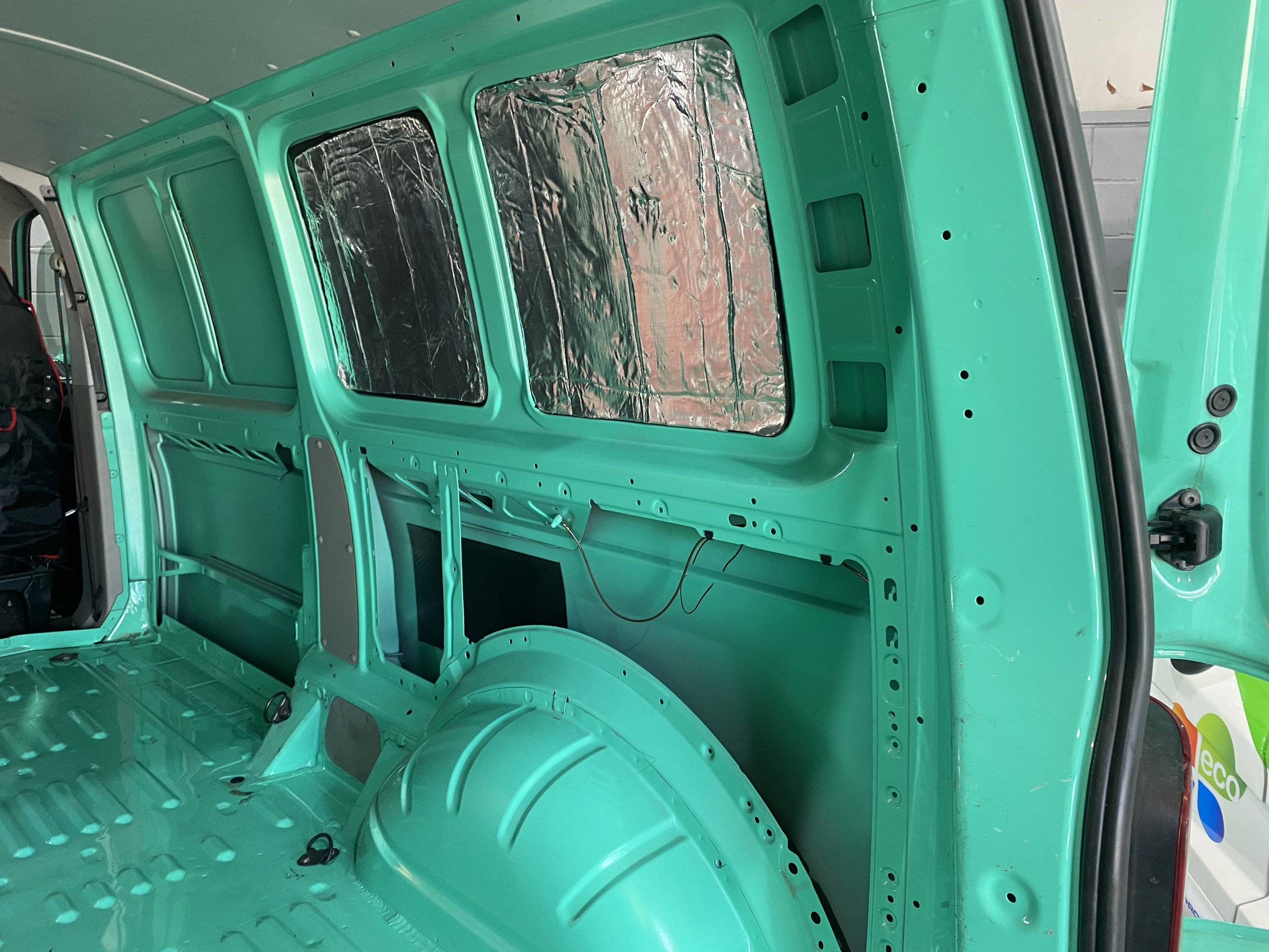 Interior of a mint green van with windows covered in reflective insulation material.