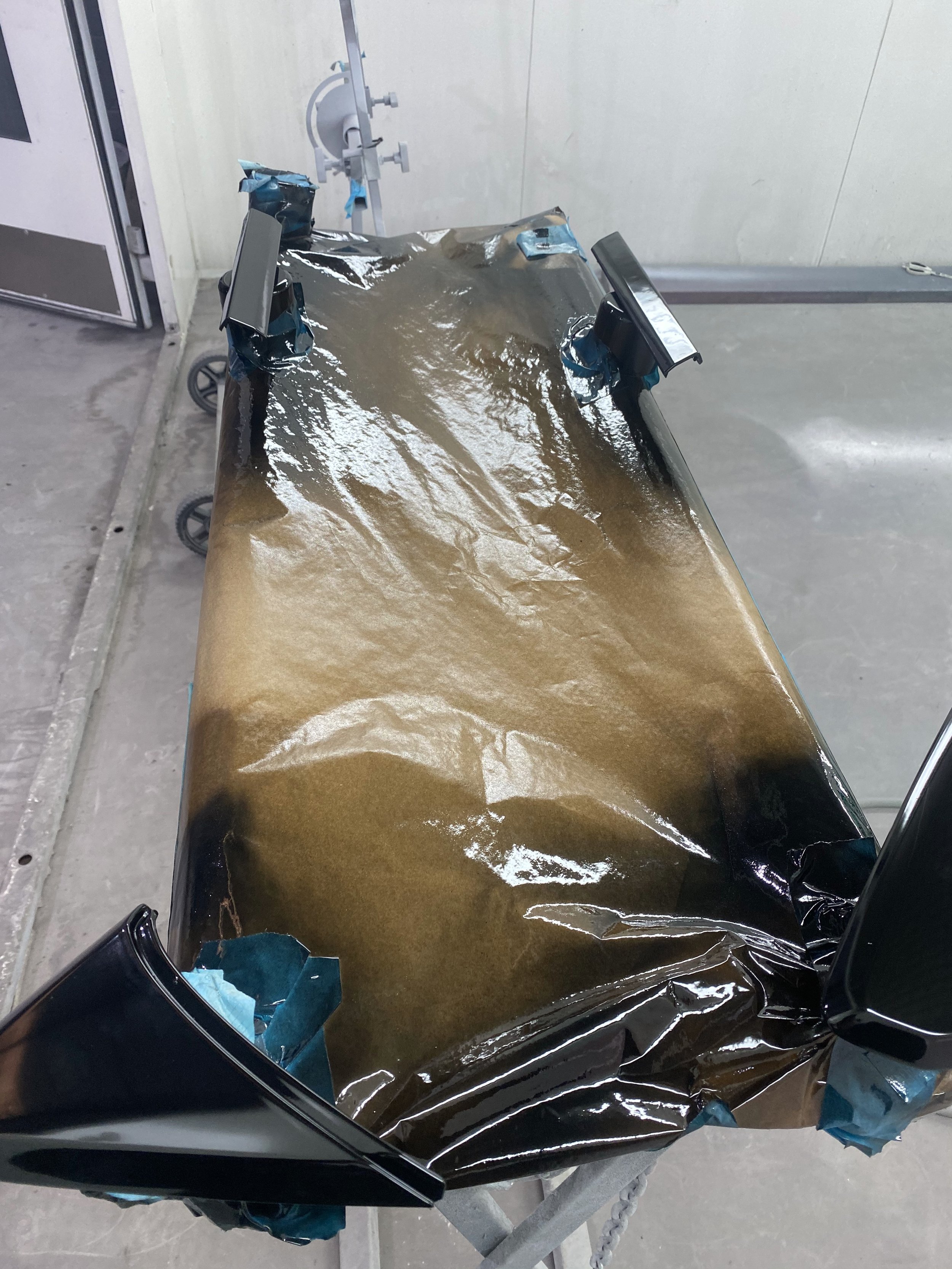 A worktable covered with a sheet of brown protective paper, taped down with blue painter's tape at the edges and around supports, in a workshop or paint booth.