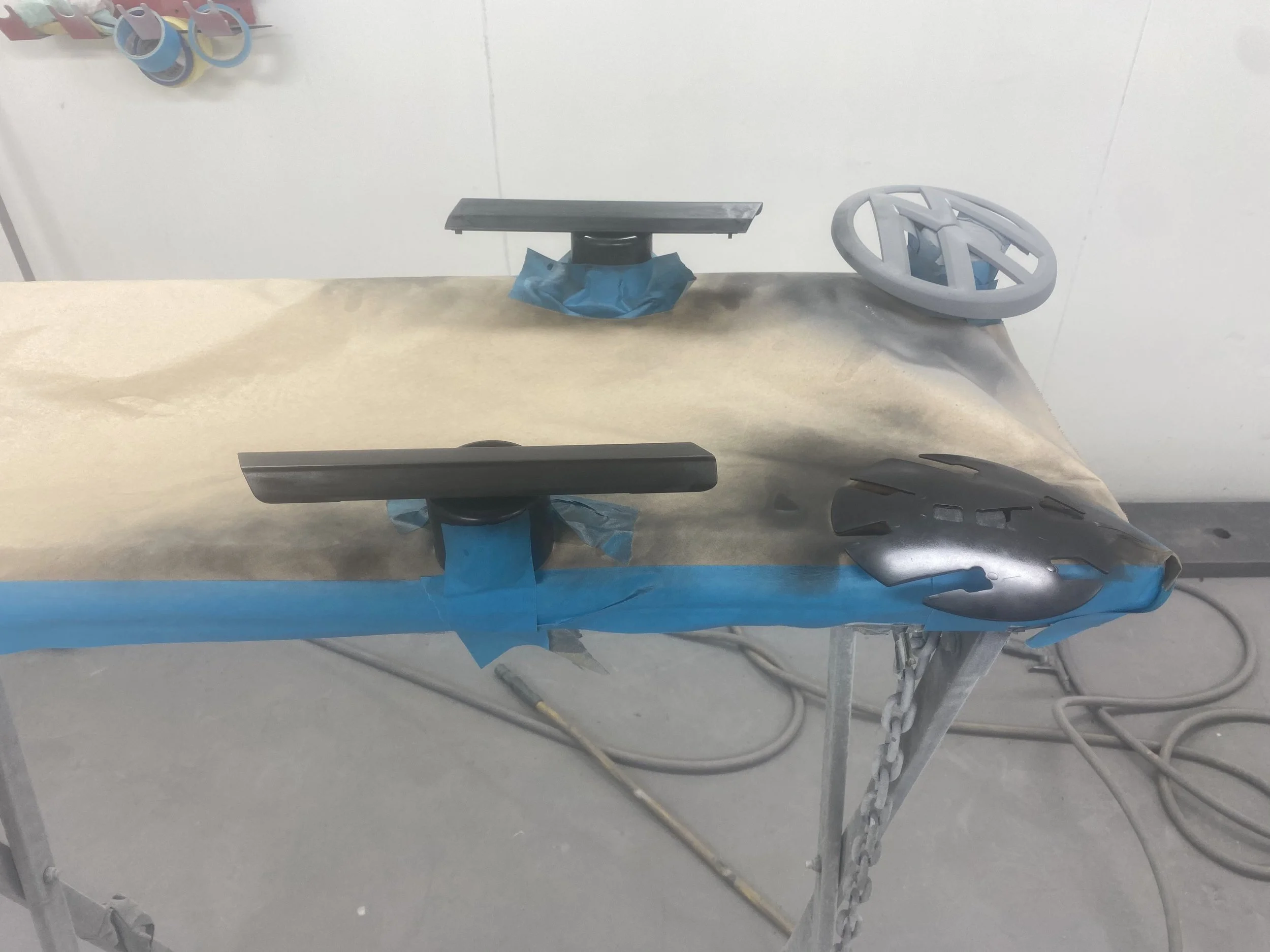 Car steering wheel, dashboard, and other parts covered with masking tape and paper, placed on a work table prepared for painting.