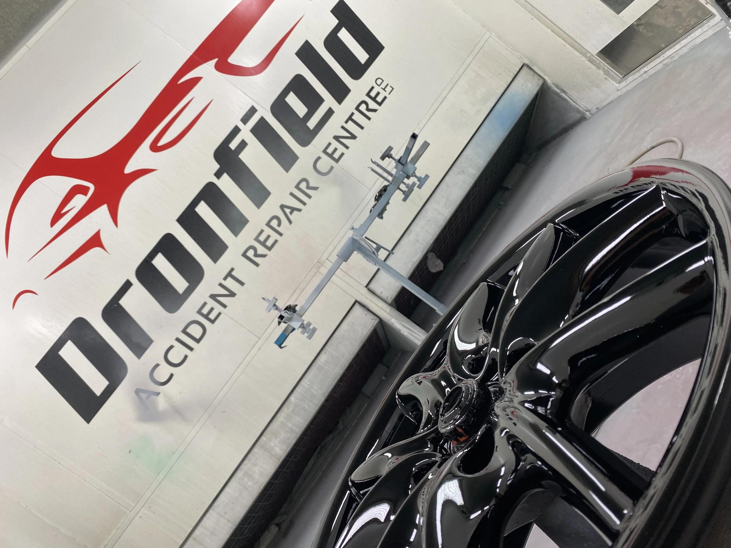 A shiny black car wheel in front of a wall with the Red Dragon logo and the text 'DION DIT' and 'Accident Repair Centre'.