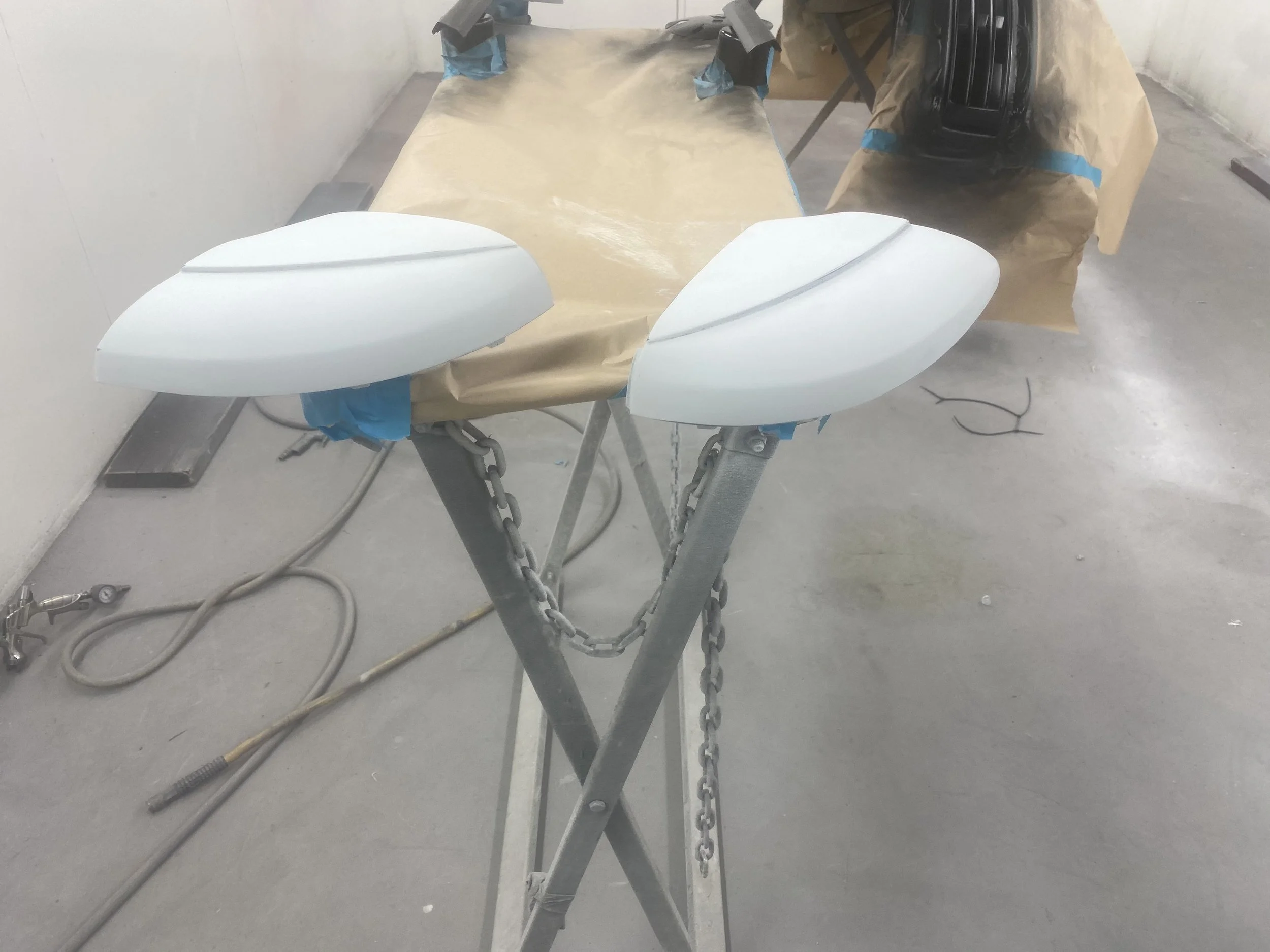 Two new white motorcycle fairings sitting on a work table covered with brown paper, with tools and equipment around in a workshop.