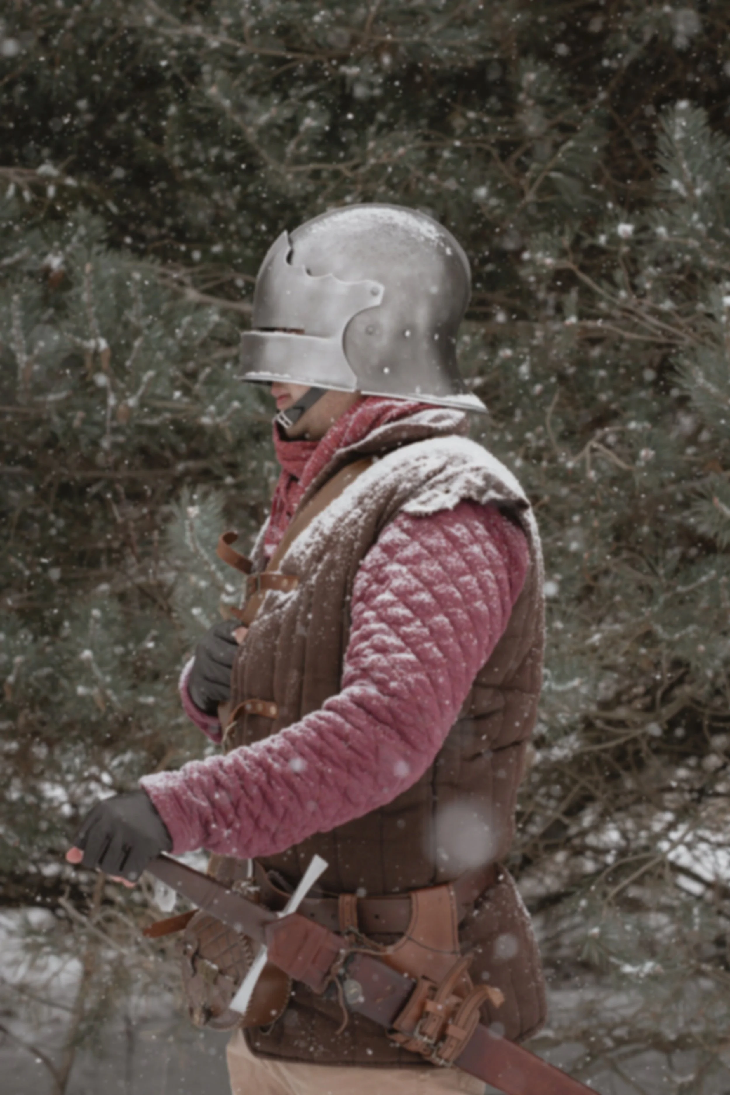 Man wearing a vintage helmet, clothes and gloves, standing in a snowy forest with snow falling.