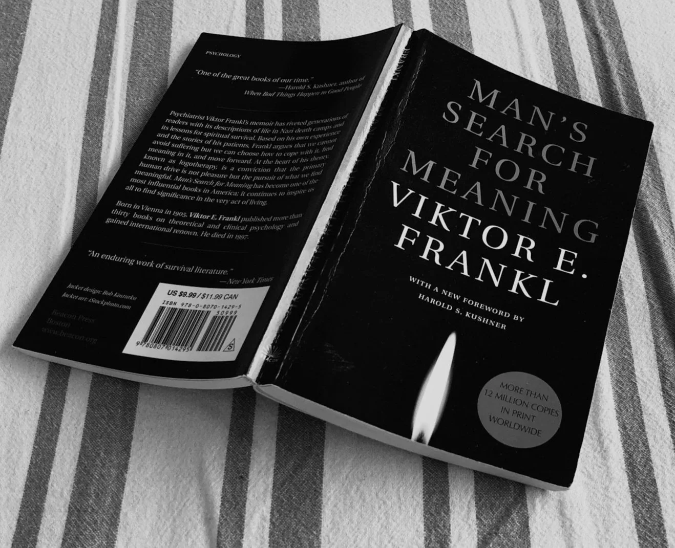 A black and white paperback book titled 'Man's Search for Meaning' by Viktor E. Frankl, with a foreword by Harold S. Kushner, lying on striped fabric.