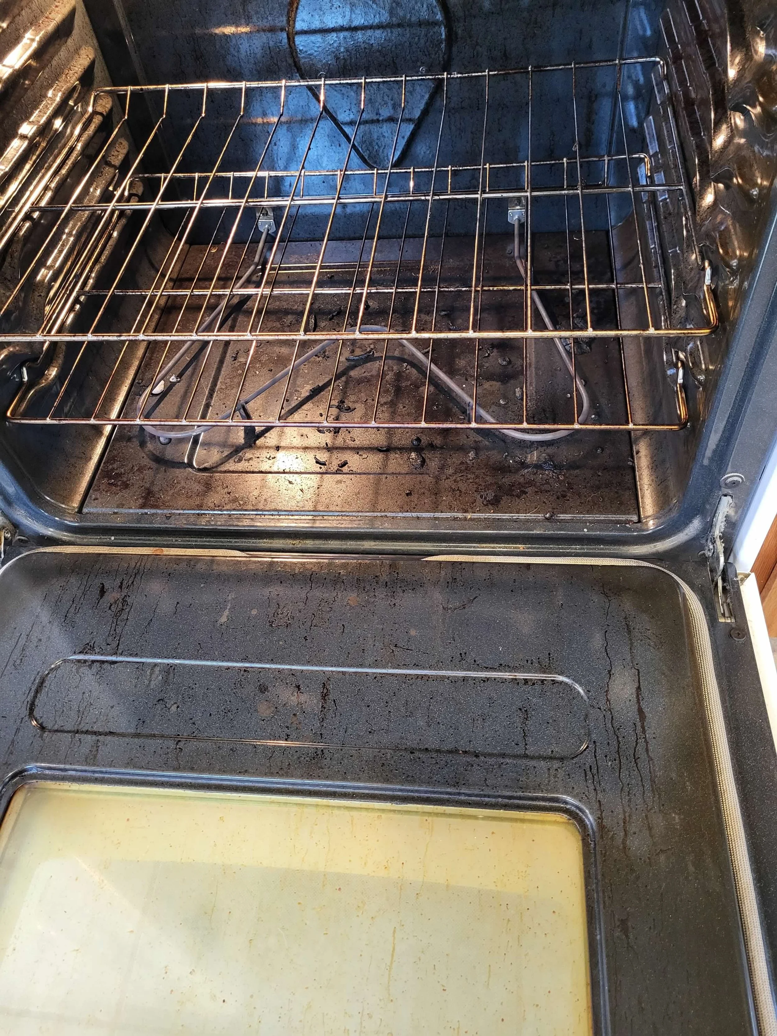 Inside of an oven with a metal rack, some black soot and grime on the oven floor, and a glass tray at the bottom.
