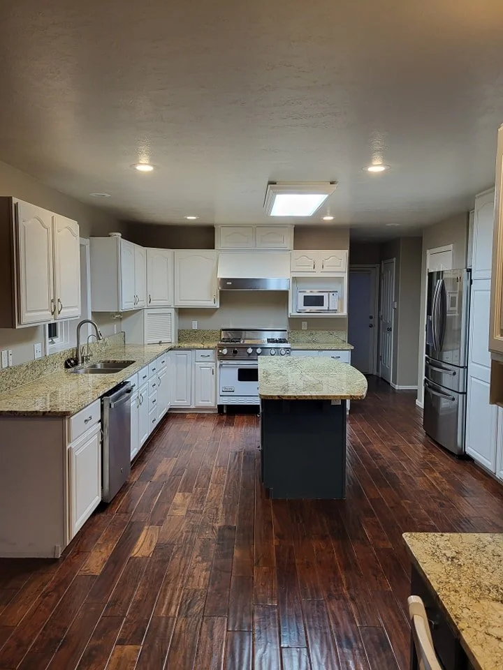 Kitchen with white cabinets, granite countertops, stainless steel appliances including a refrigerator, oven, microwave, and dishwasher. Dark wooden flooring and a central island with a matching granite top.