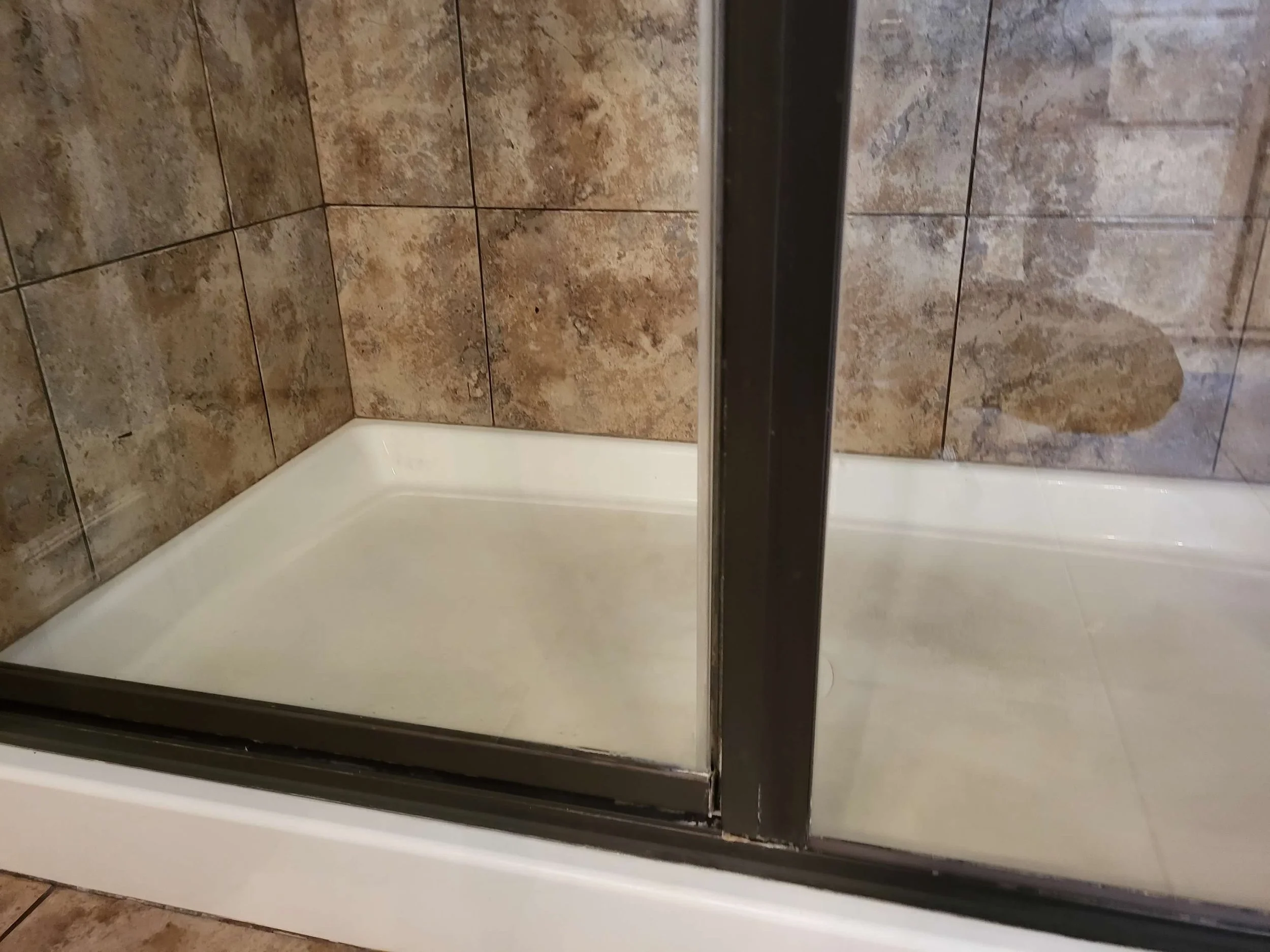 A close-up of a shower with a glass door and brown stone tiles on the walls. The shower tray is white.