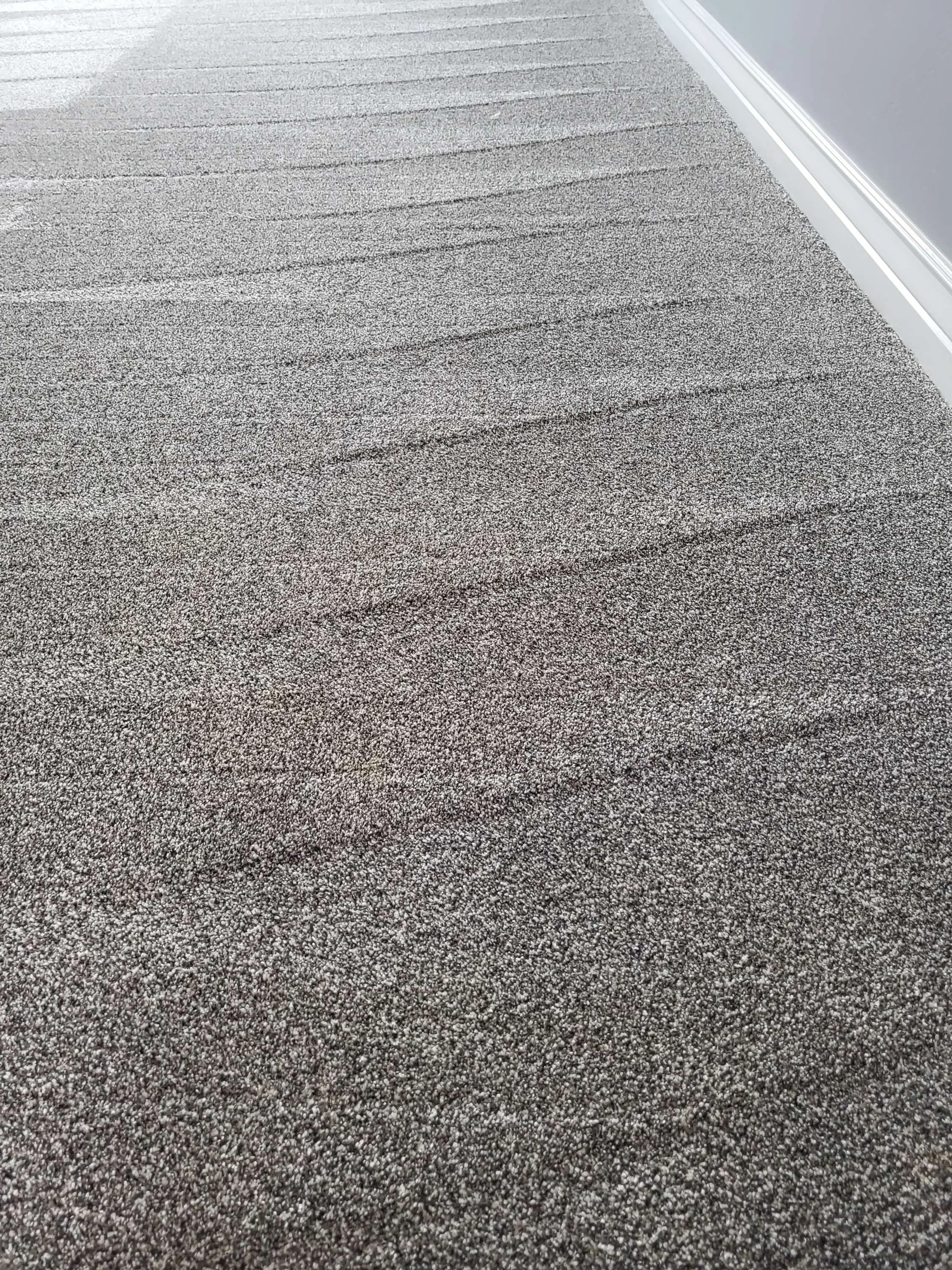 Close-up of a textured gray carpet on a floor near a white wall.