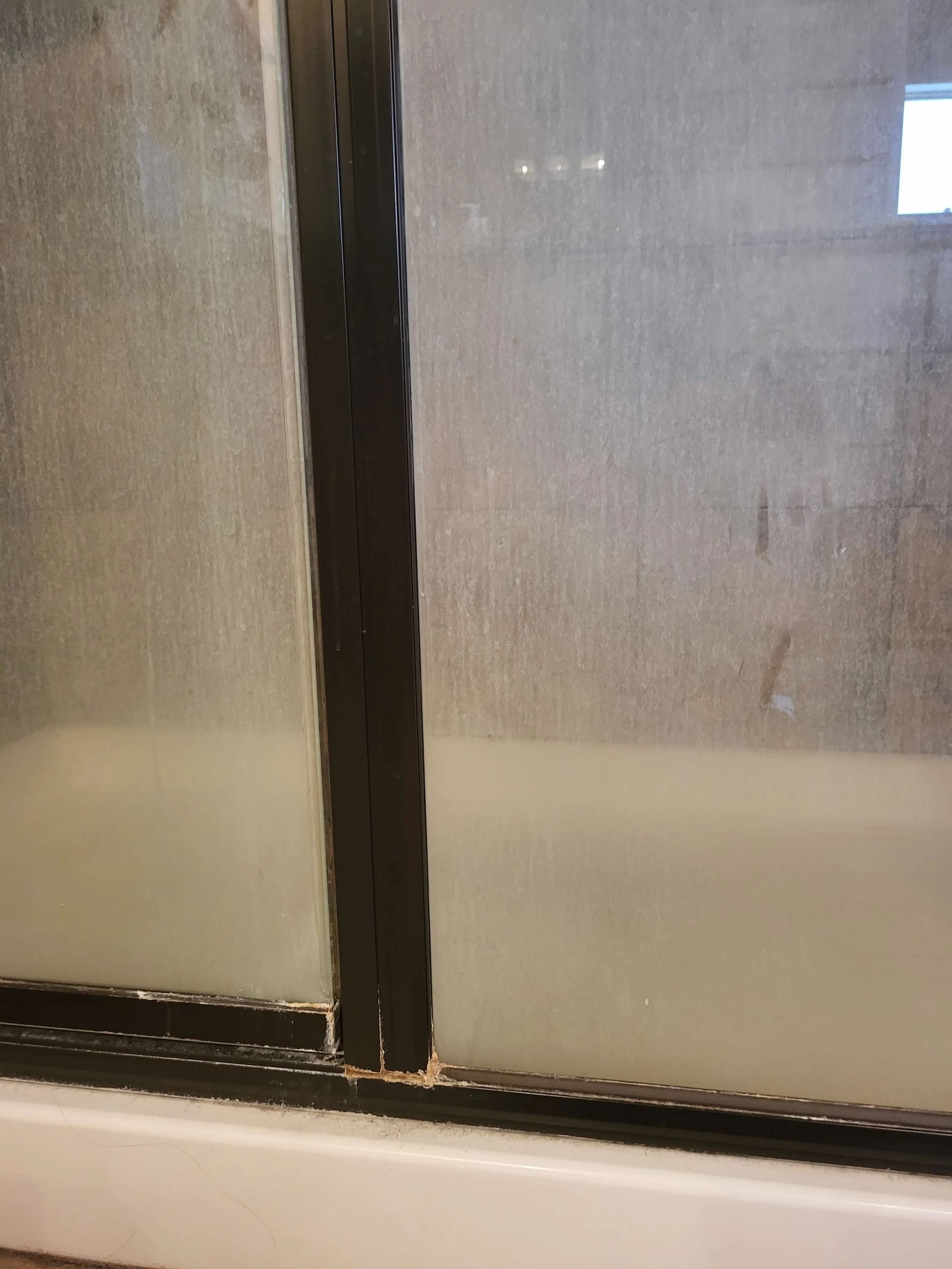 Close-up of a sliding glass door with dirt and grime along the bottom edge, showing a reflection of an indoor space with a window.