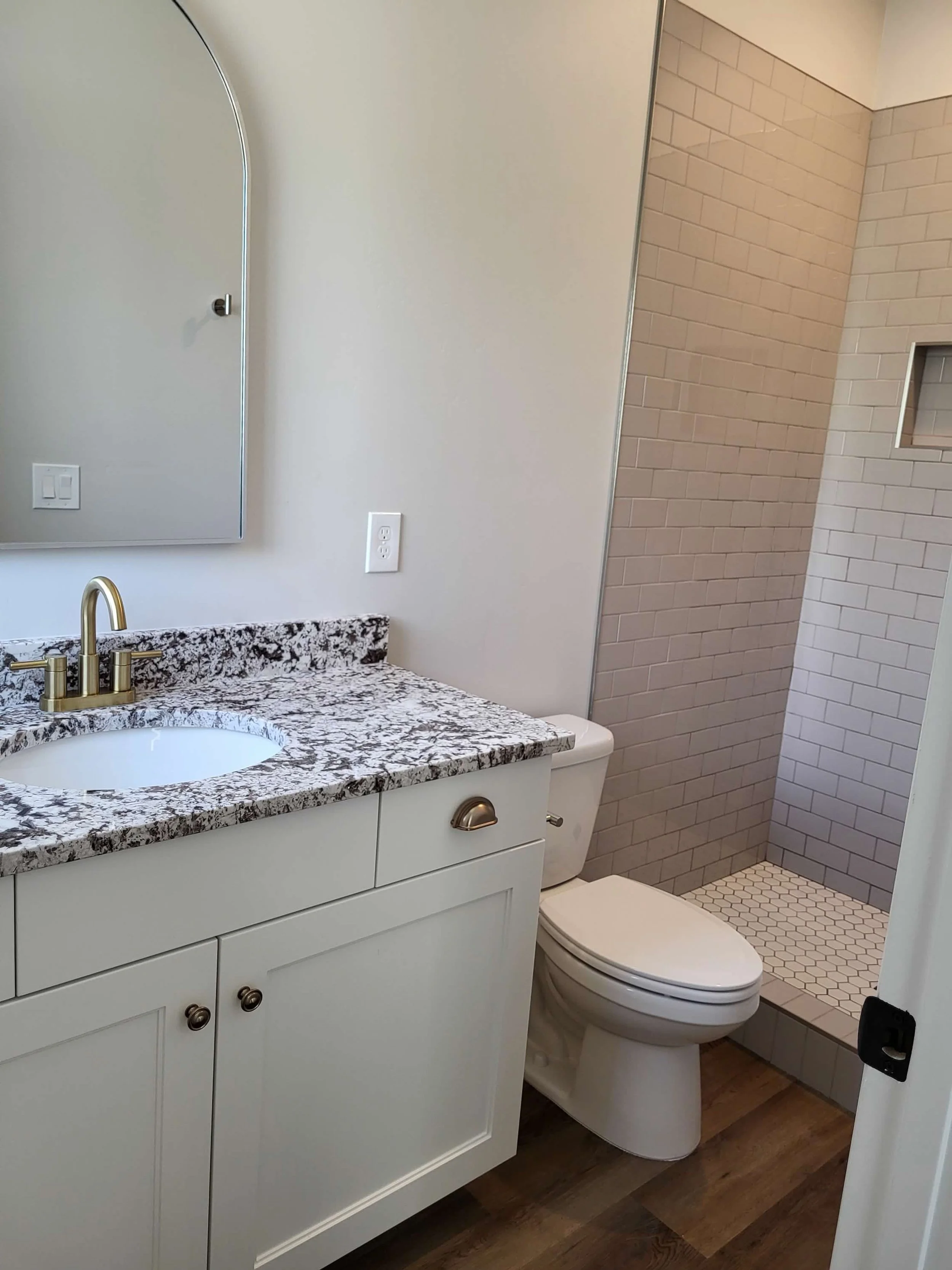 Bathroom with a white vanity, granite countertop, oval mirror, and a walk-in shower with beige subway tiles.