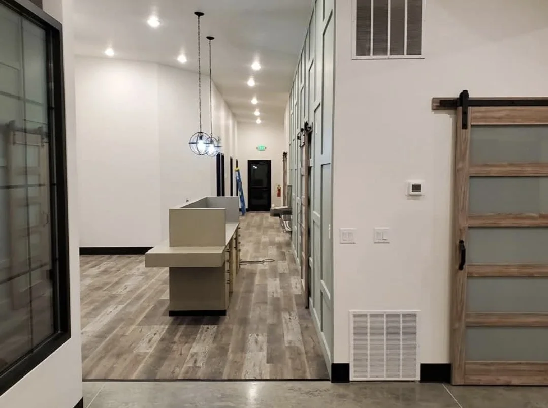 Interior view of a modern kitchen and living area with light wood flooring, white walls, hanging pendant lights, and a sliding barn door.