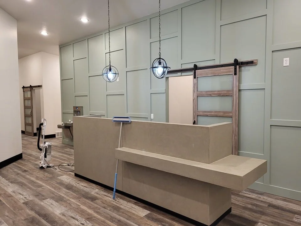 Empty reception desk in a modern space with green paneled walls, two hanging light fixtures, and a wooden sliding barn door.
