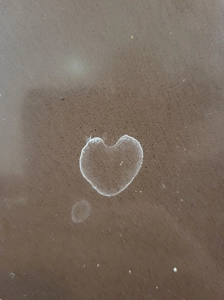 A scuffed dark surface with a prominent heart shape outline and a smaller circle nearby.