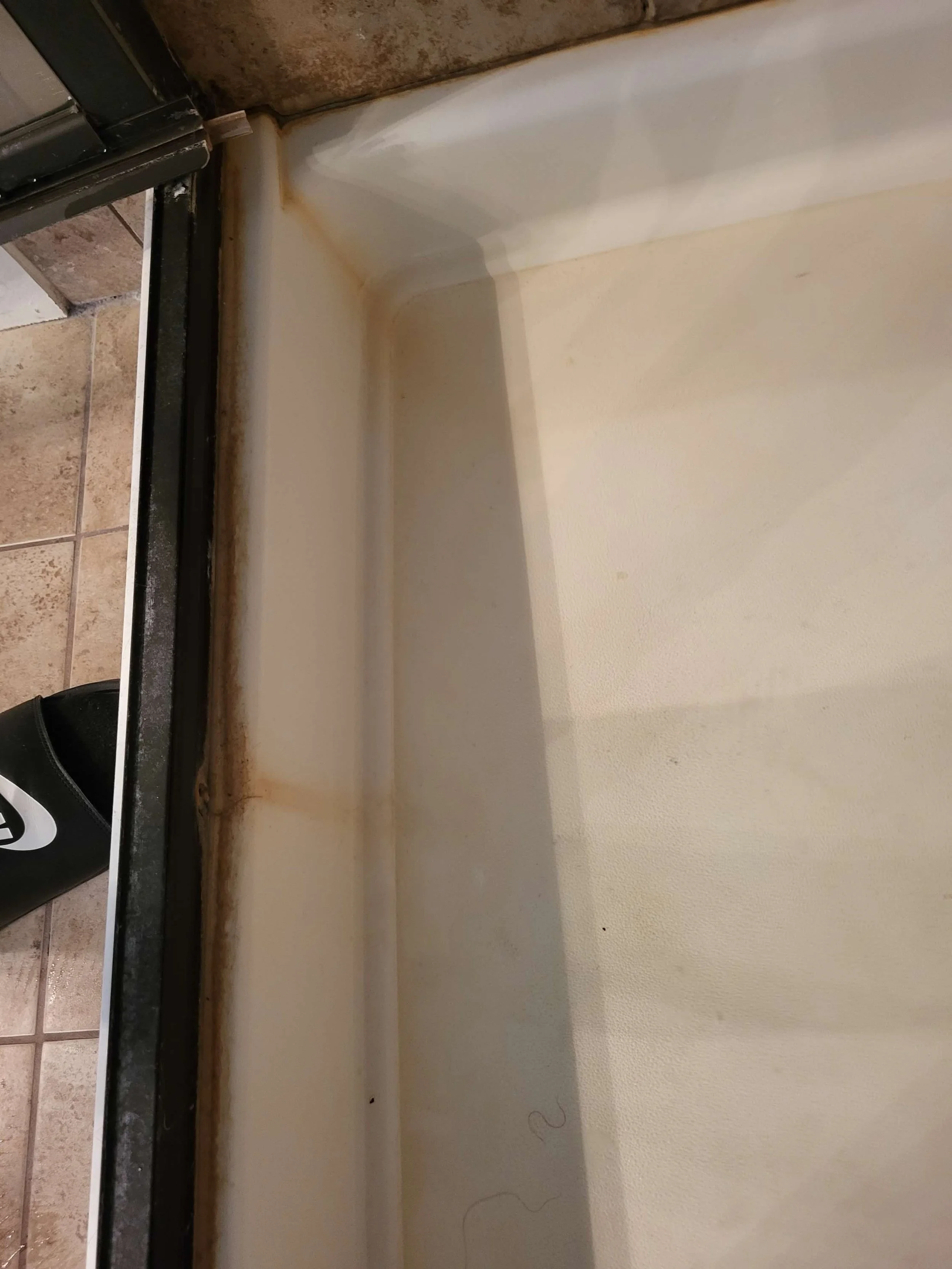 Close-up of a dirty and stained bathtub with brownish grime along the edges and corners.