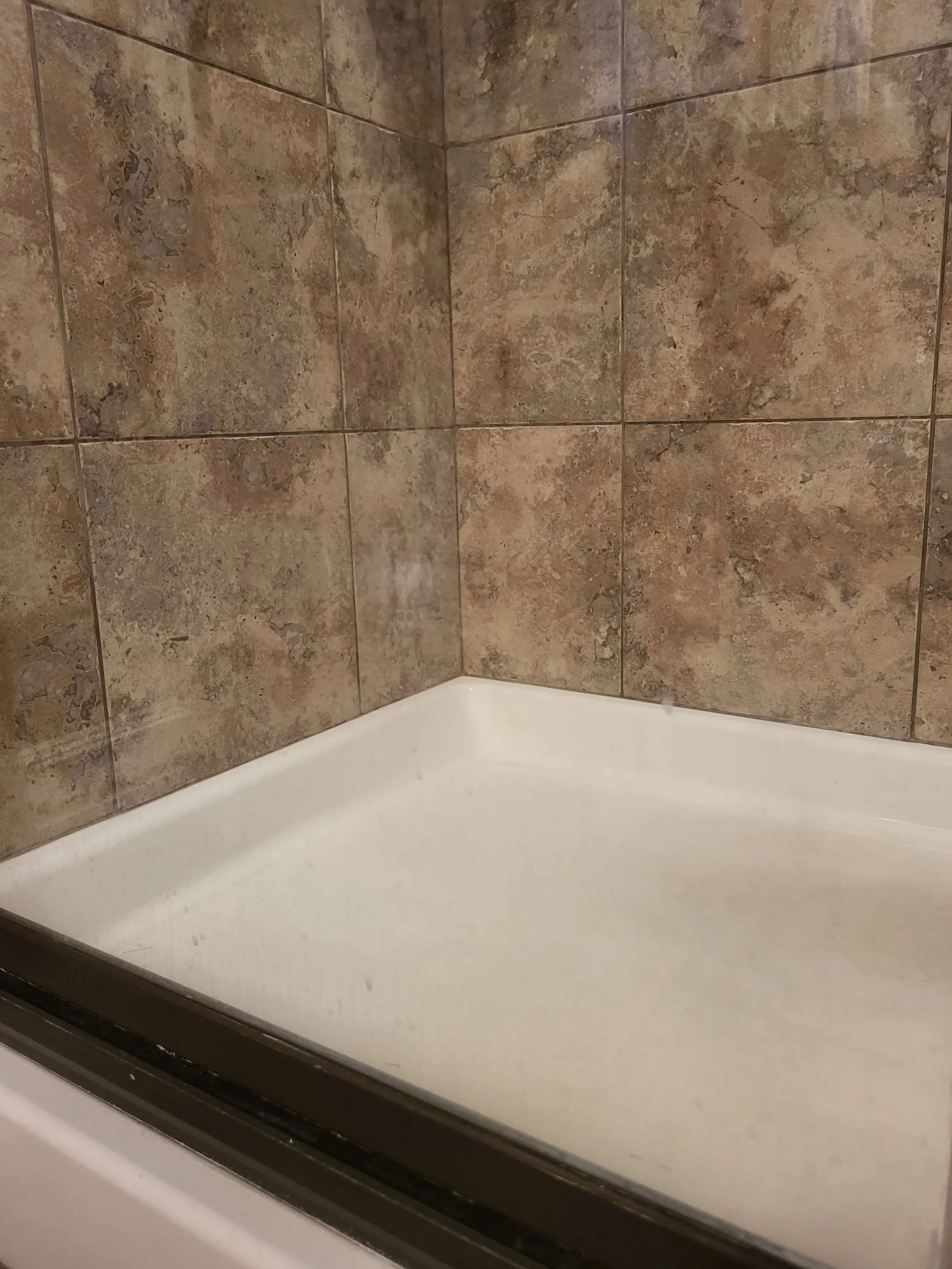 Empty bathtub surrounded by brown tiled walls.