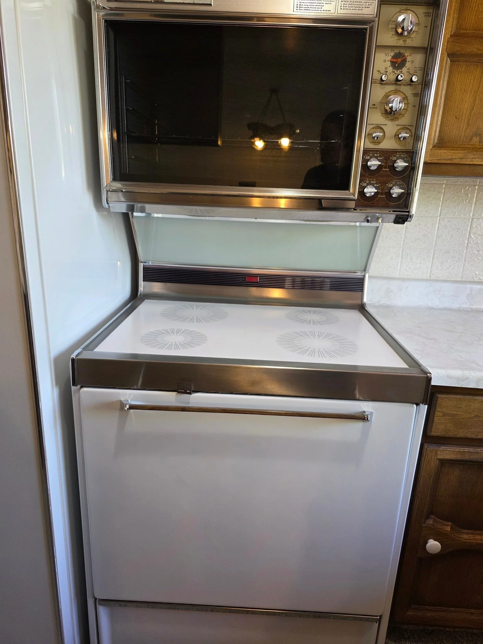 A vintage kitchen oven and stove combination with a top oven and a white cooktop, positioned between wooden kitchen cabinets.