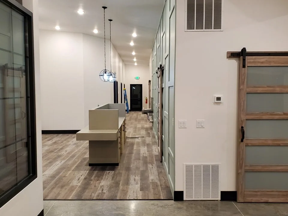 Interior view of a modern, minimalistic space with wood flooring, pendant lighting, a wooden sliding barn door, and a white wall.