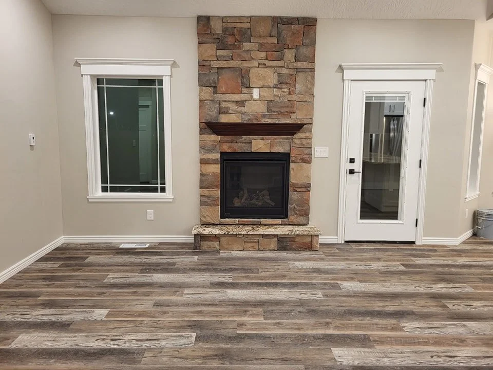 Living room with a stone fireplace, wooden mantel, window, and glass door leading to the kitchen.