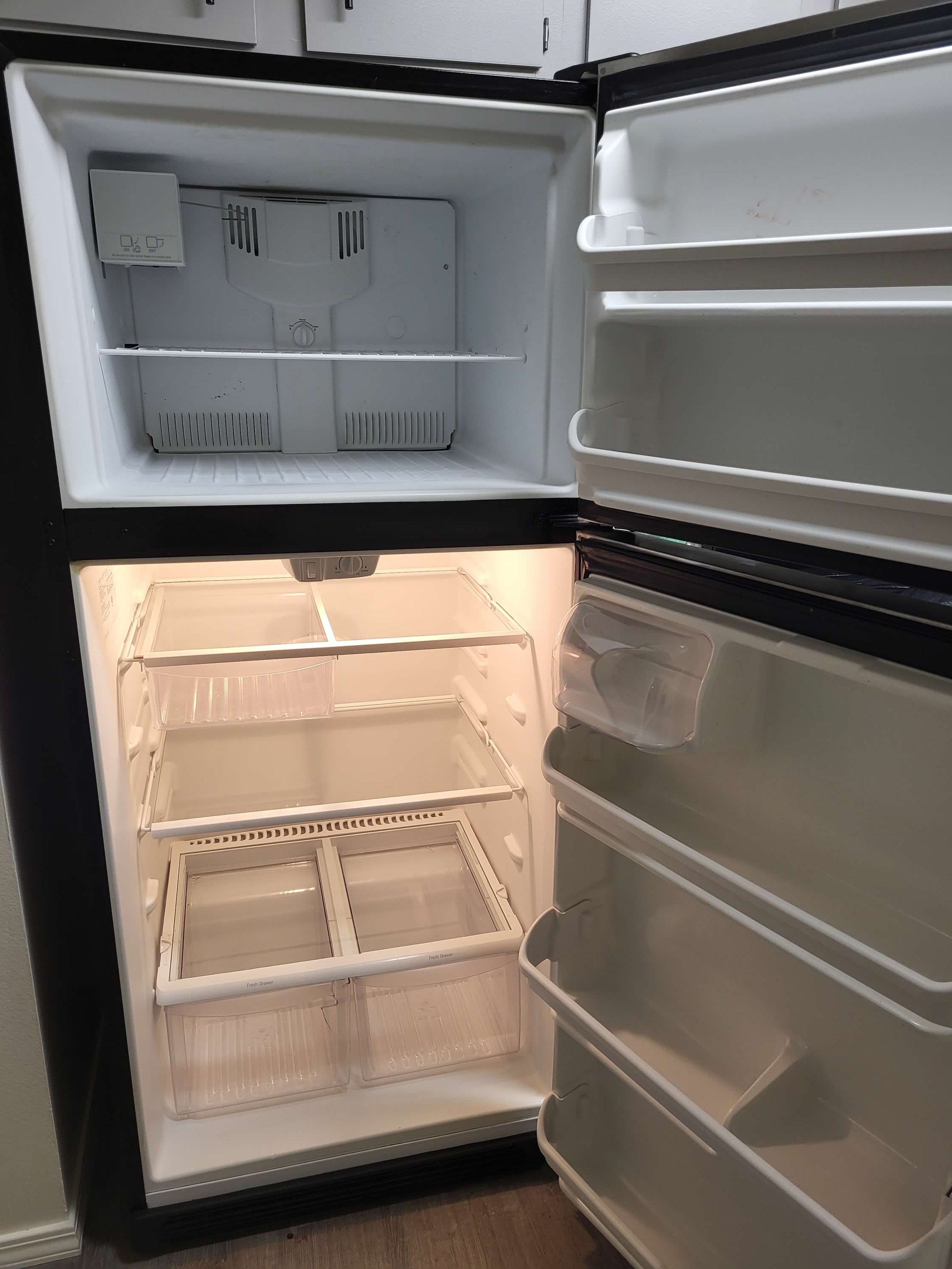 Empty black refrigerator with open door showing interior compartments and shelves, light on inside, with nothing stored inside.