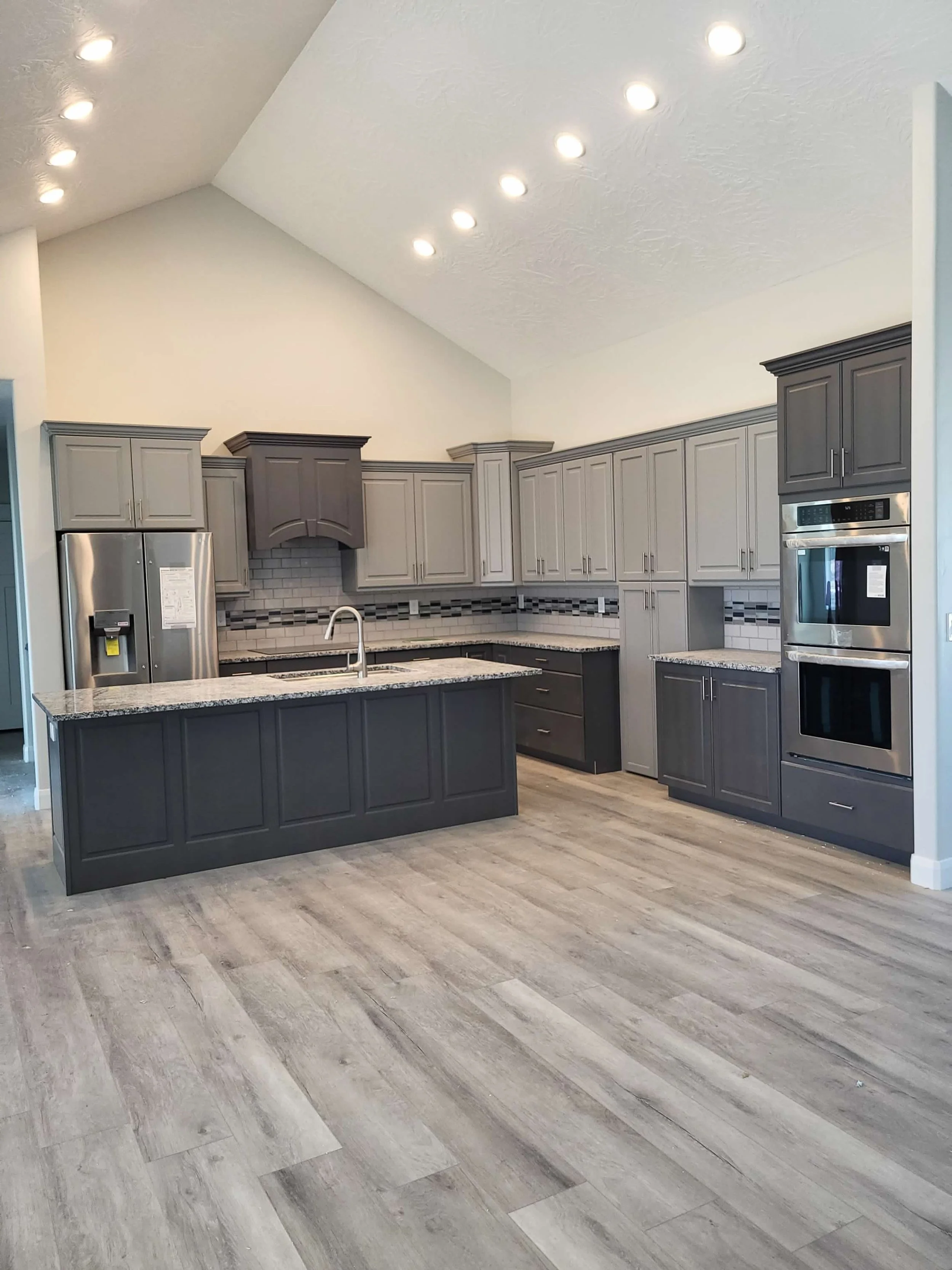 Modern kitchen with gray cabinets, granite countertops, stainless steel appliances, and a wooden floor.