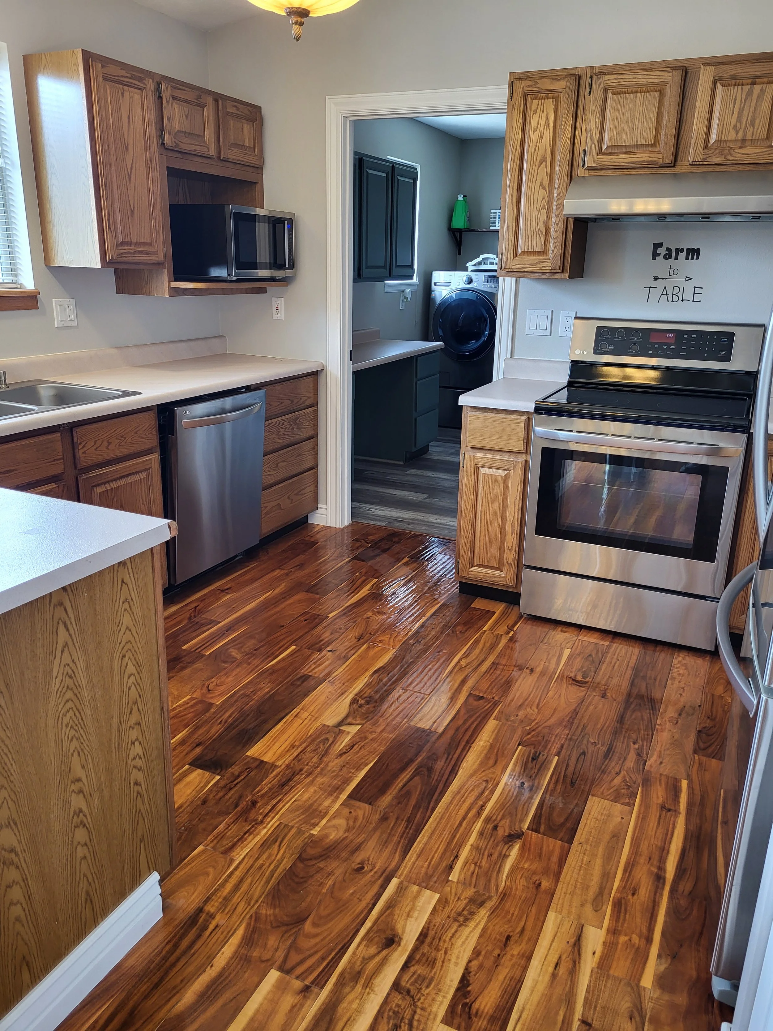 Kitchen with wooden cabinets, stainless steel appliances, hardwood flooring, and a doorway leading to a laundry area with a washing machine.