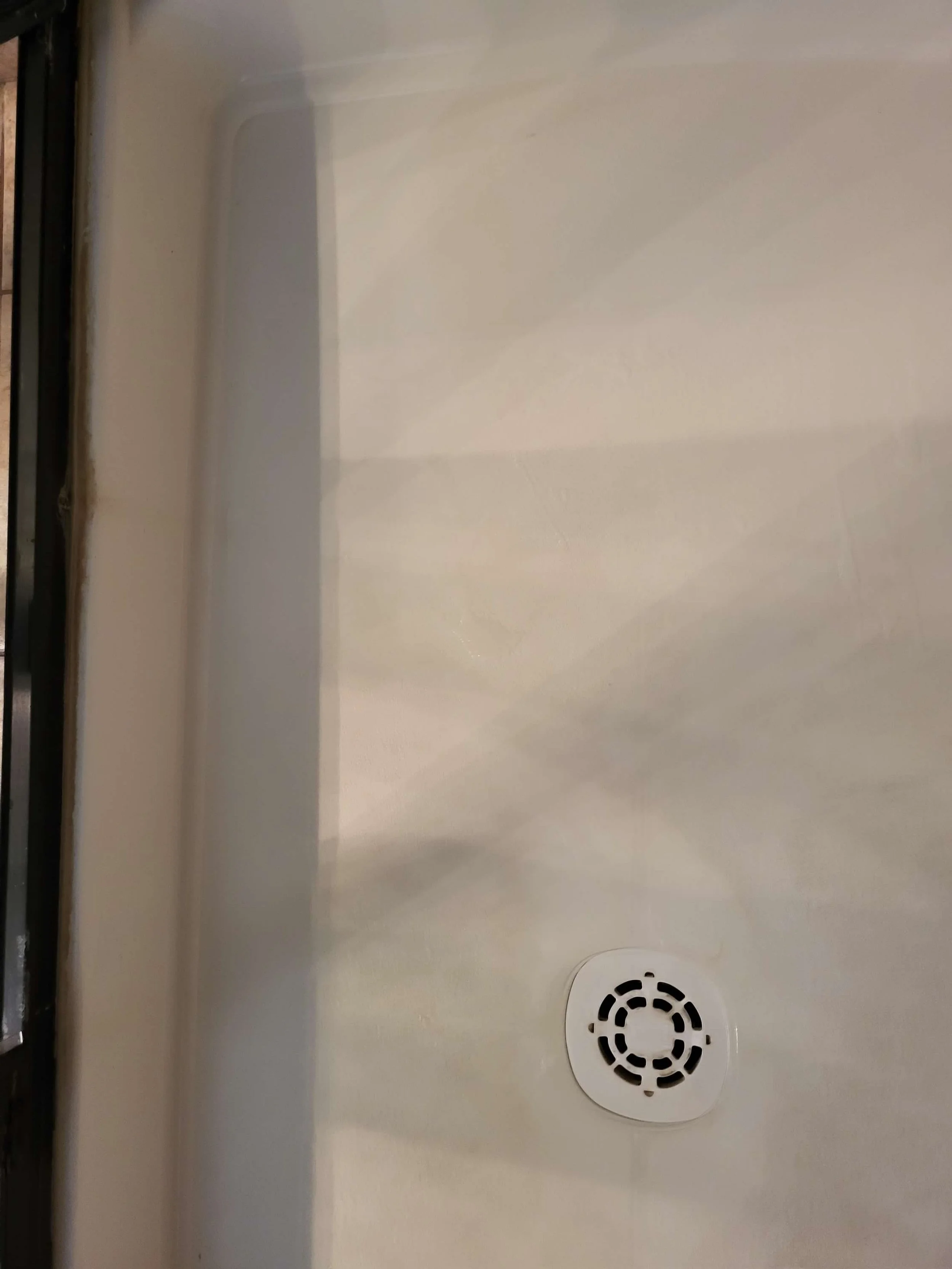 Close-up of a shower floor with a white drain cover and beige tile surface.