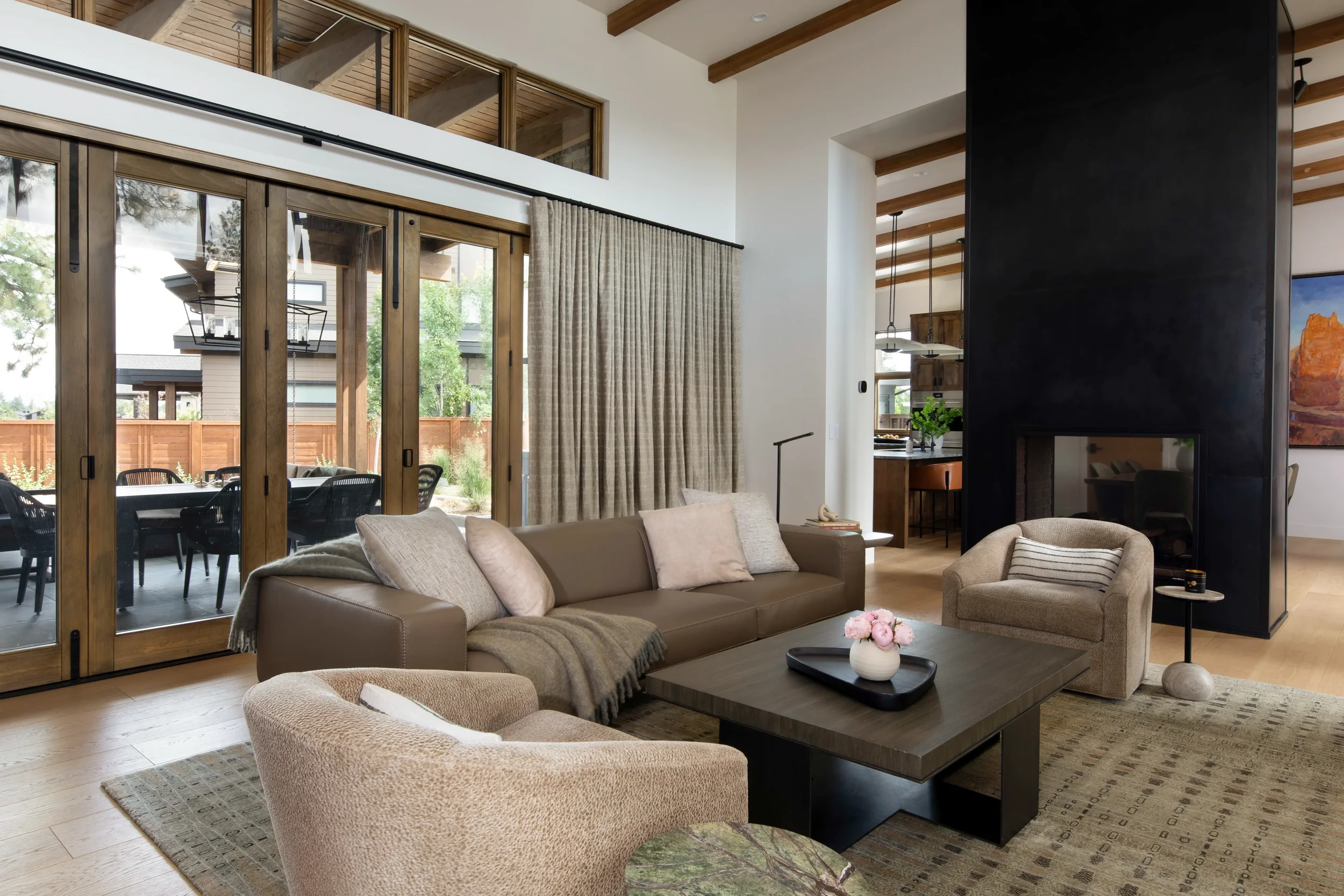 Modern living room with leather sofa, armchairs, large wood-framed glass doors, coffee table, and black fireplace