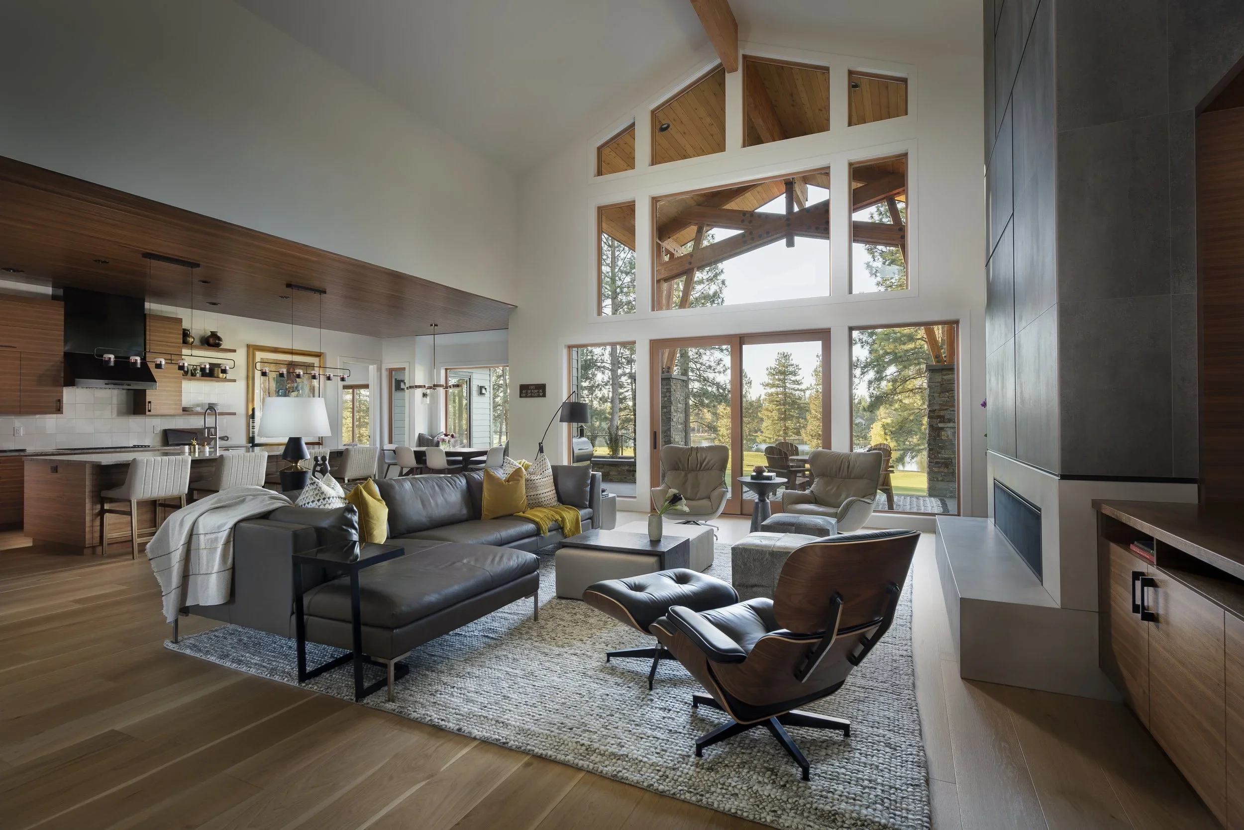 Modern living room with large windows, wooden ceiling, white walls, and seating area including a sofa and armchairs.