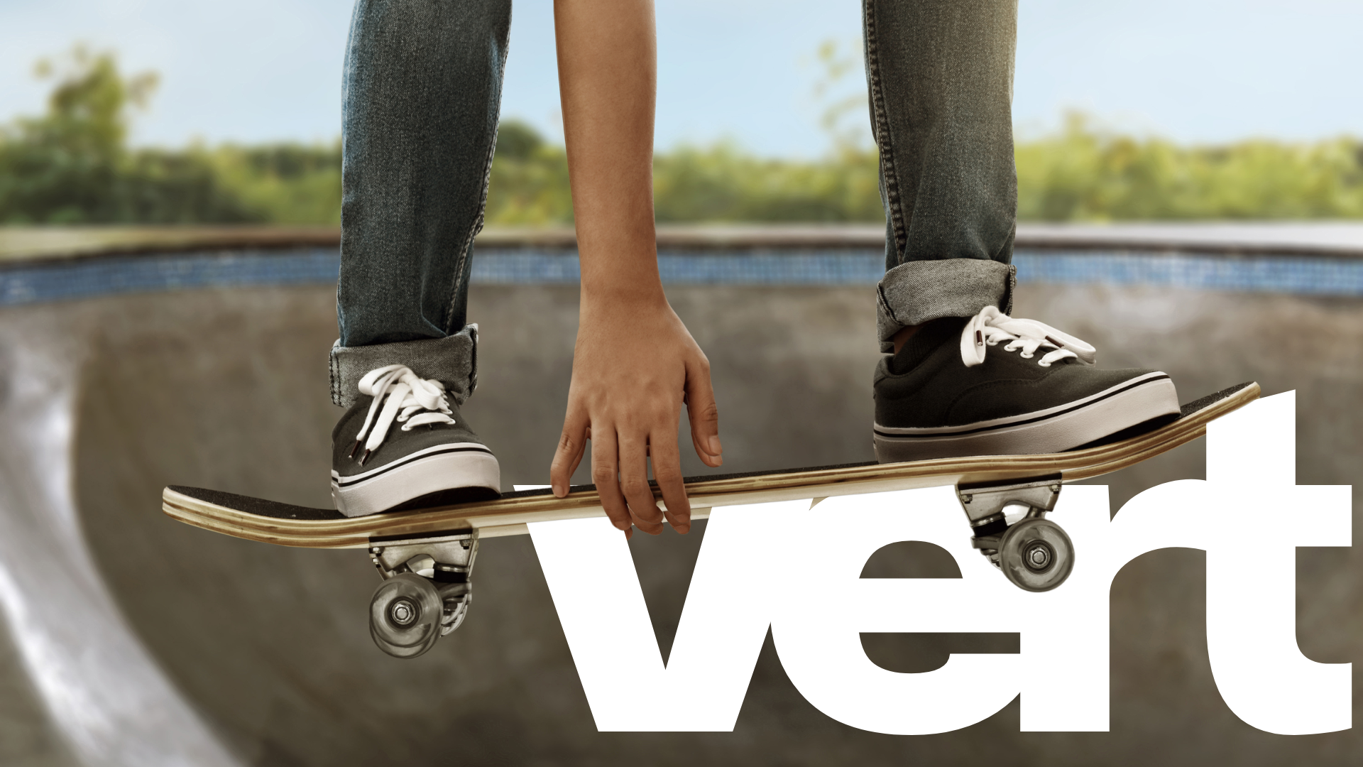 Close-up of a person skateboarding on a skatepark ramp, wearing black sneakers and jeans, with their hand touching the board.
