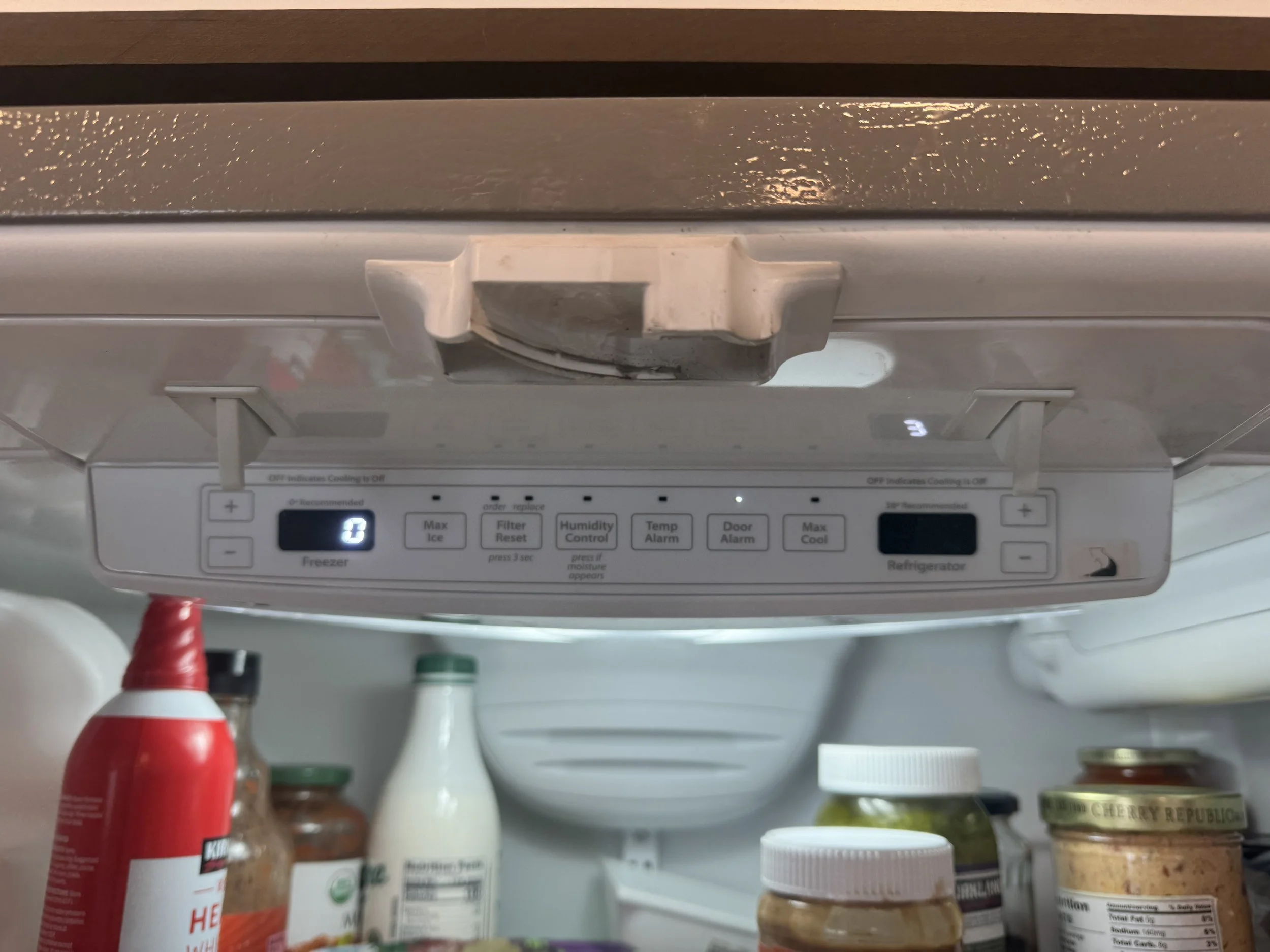 Inside refrigerator door with various condiments, jars, and bottles, with the freezer control panel visible at the top.