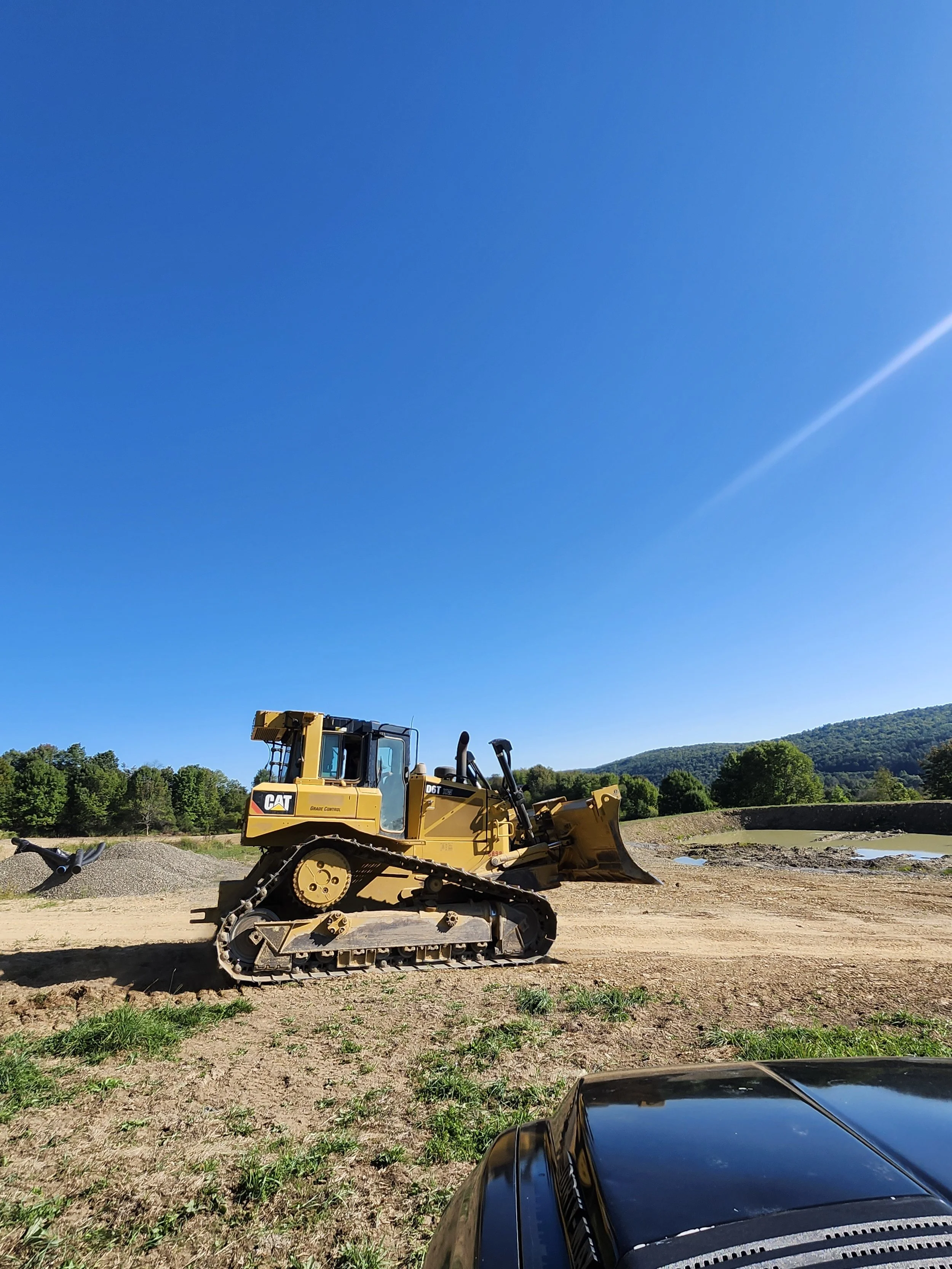 A yellow CAT bulldozer parked on a construction site with a mountain and green trees in the background under a clear blue sky.