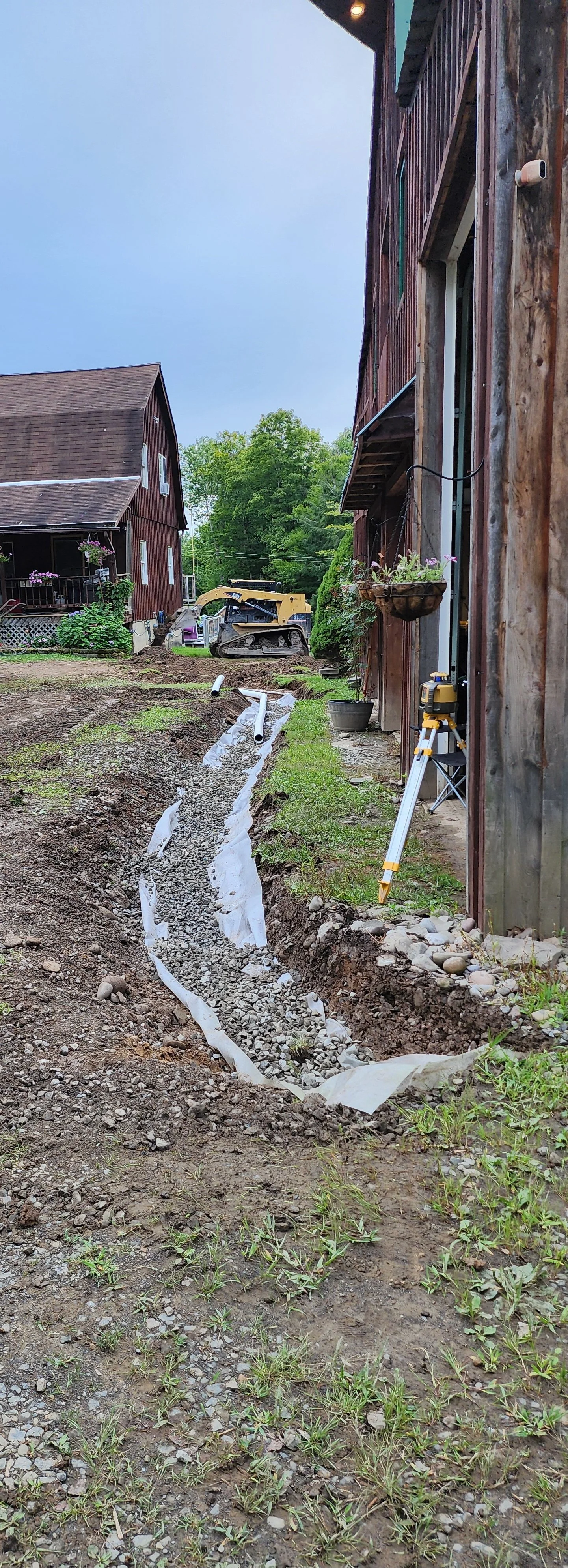Backyard undergoing trench work for plumbing installation, with construction equipment and a level tool visible.