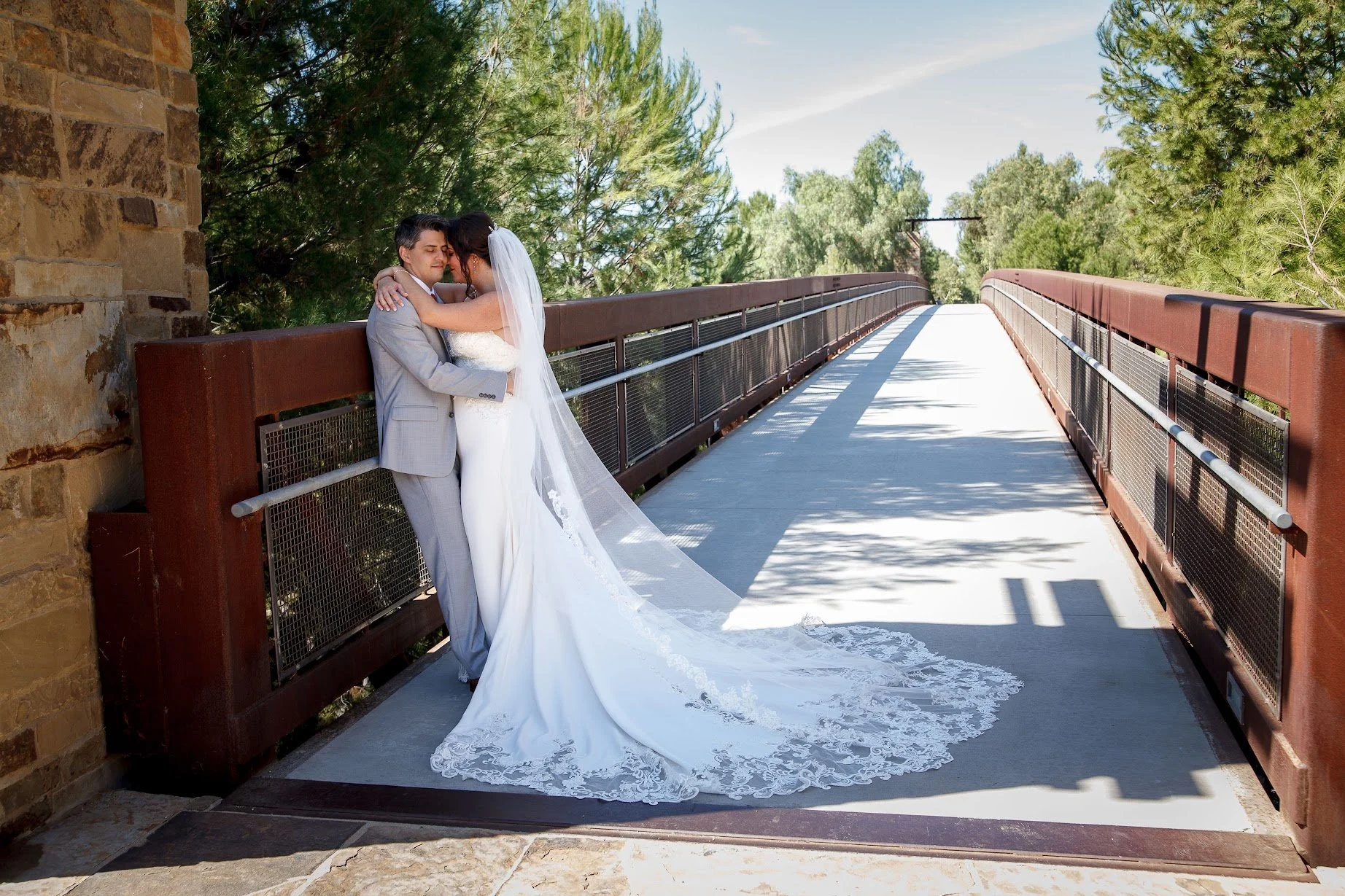 A bride and groom embracing on a bridge outdoors