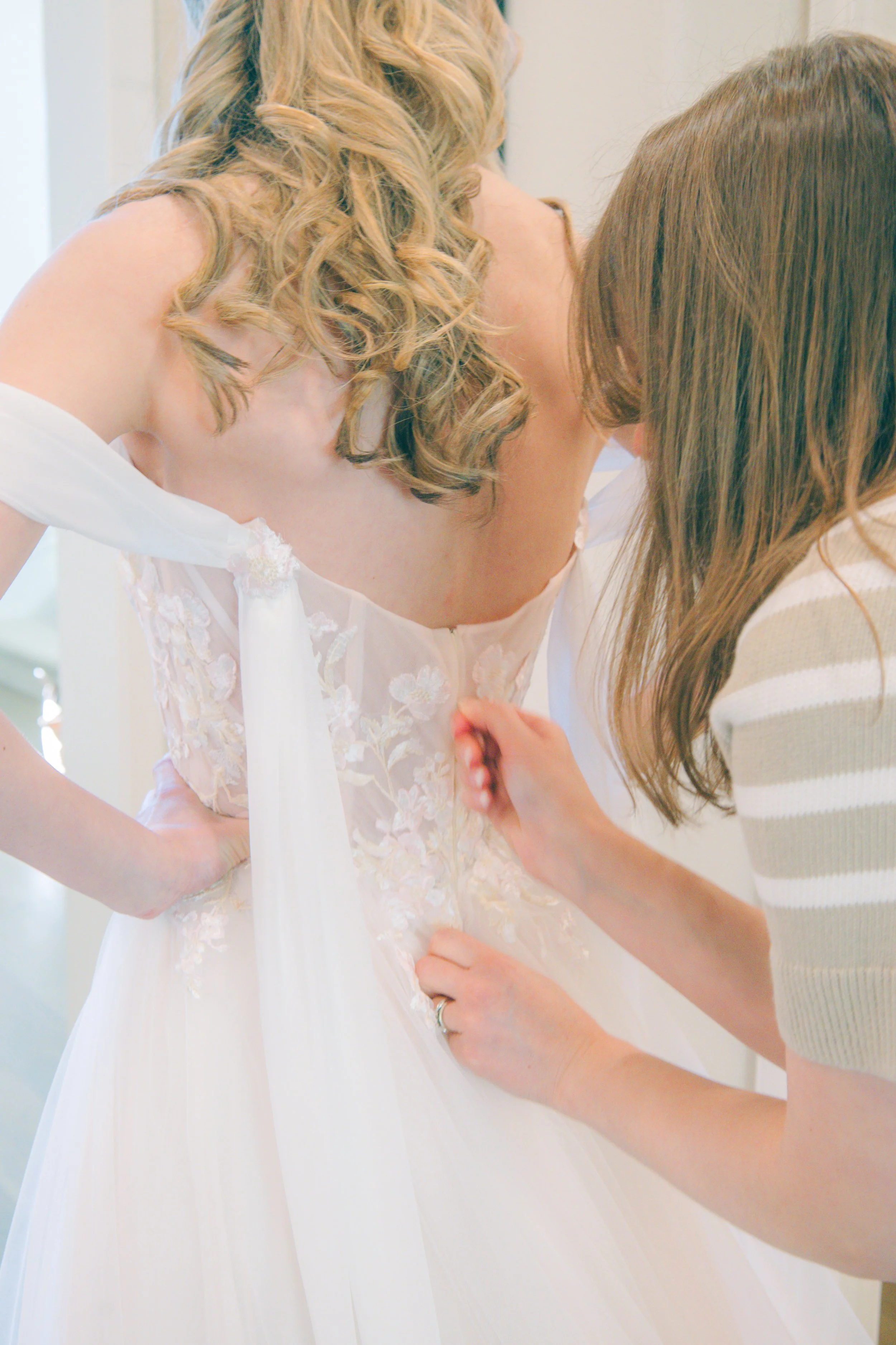 A bride getting her wedding dress adjusted by a woman.