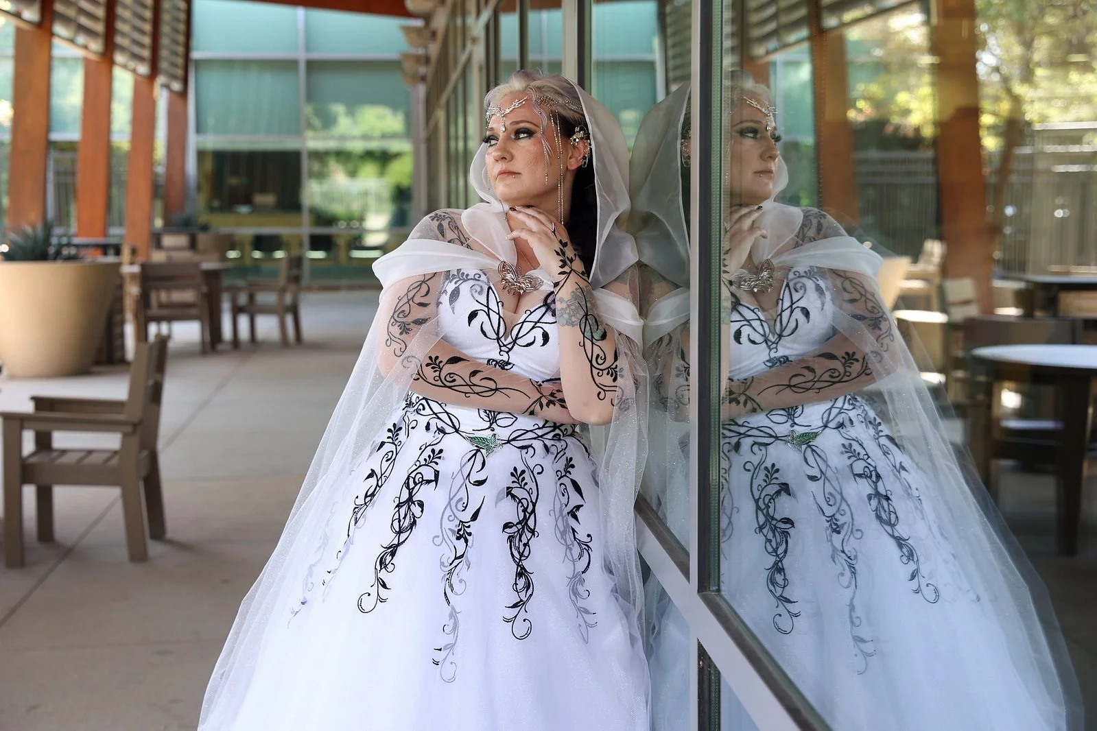 A woman wearing a white wedding dress with black embroidery, a veil, and jewelry